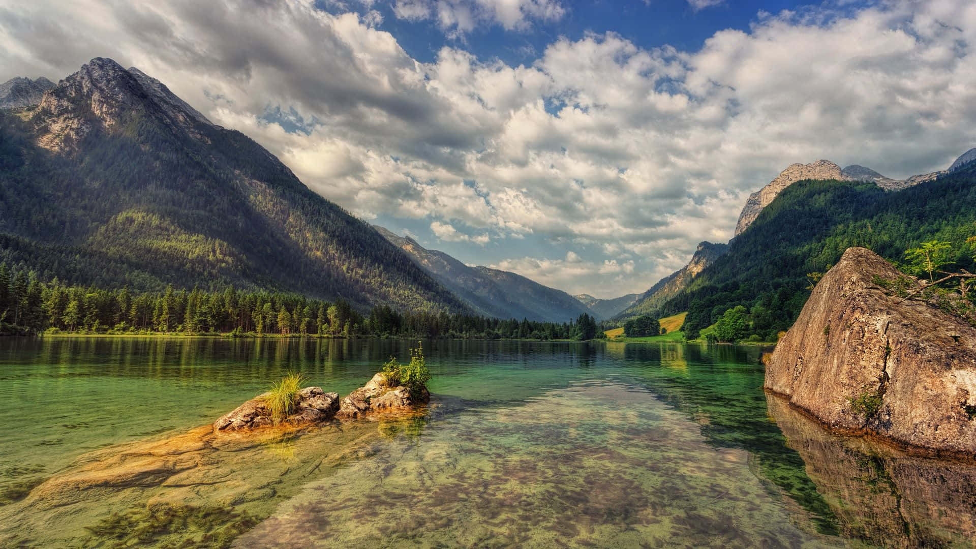 Beautiful Lake 桌布 壁紙 — 寧靜的山湖映照著高聳的綠色森林和戲劇性的雲彩，在明亮的藍天下。
