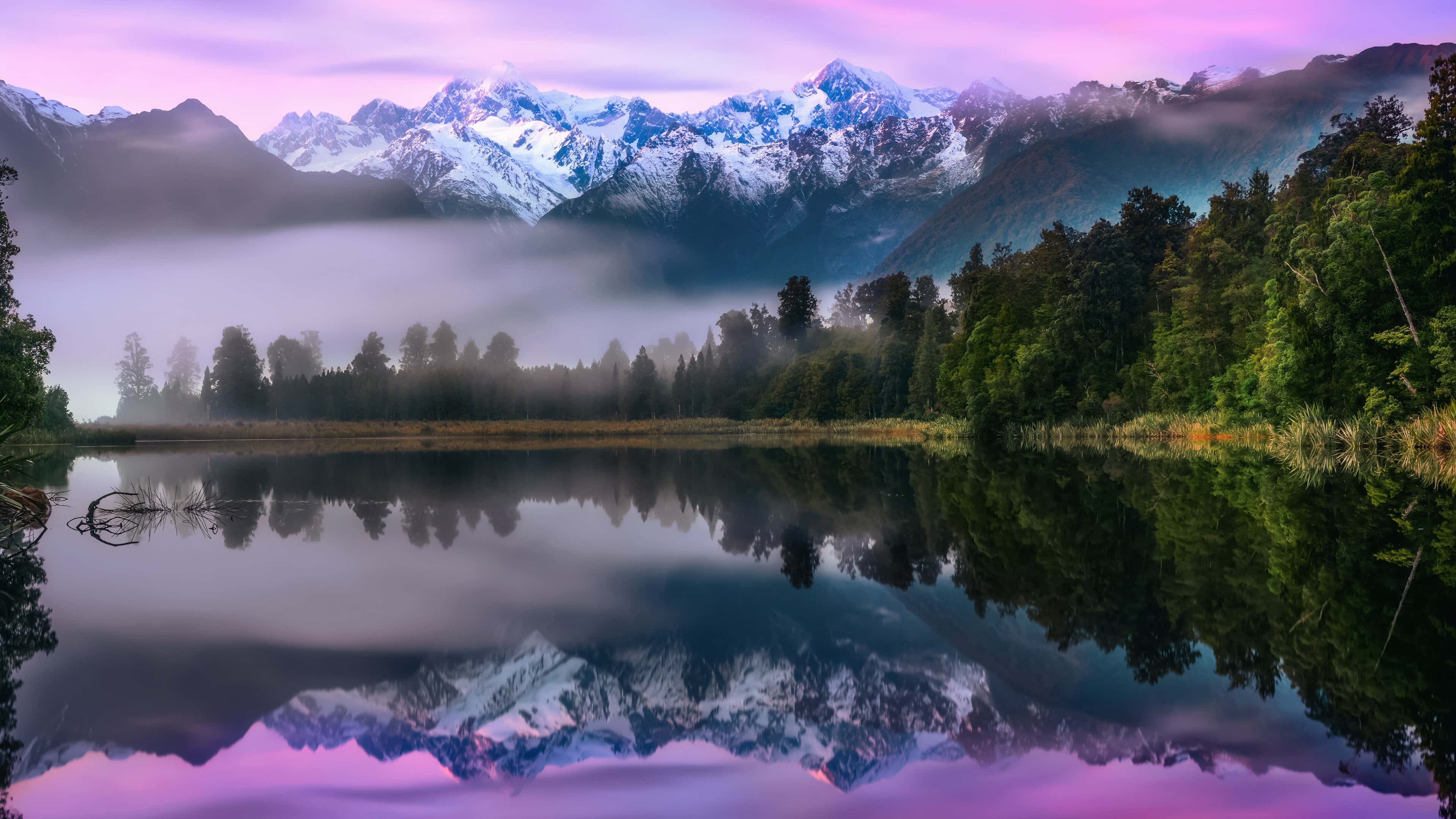 Nature Landscape 桌布 壁紙 — 寧靜的山湖透過霧氣繚繞的森林樹木，映照出白雪覆蓋的山峰和紫色的黎明天空。