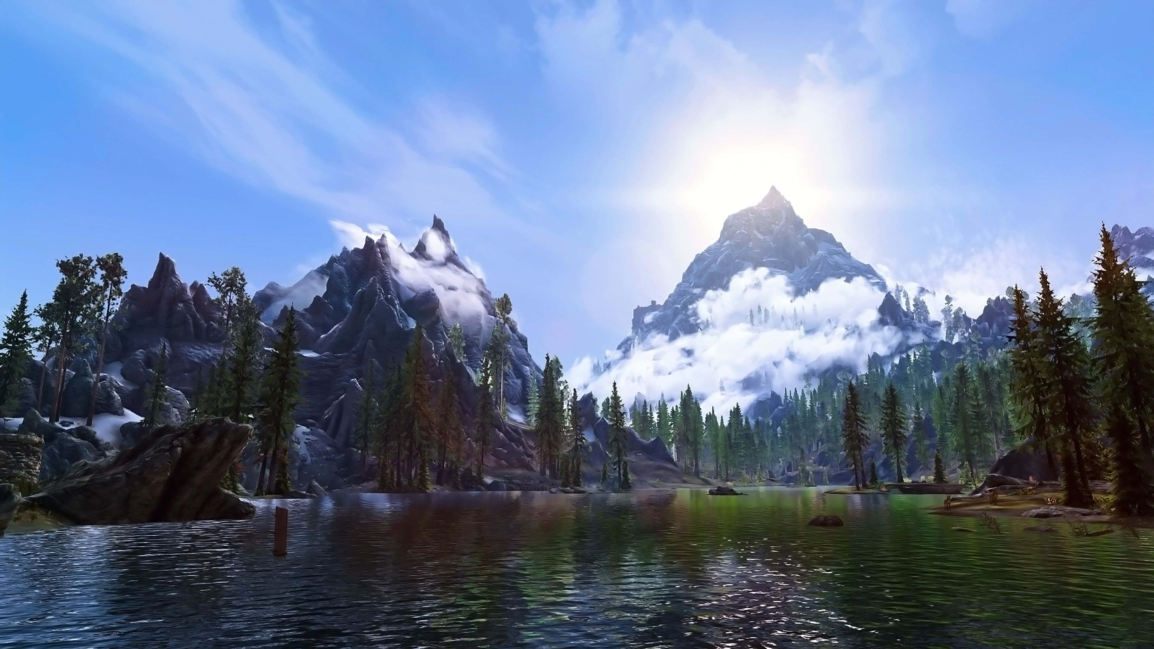 Skyrim Landscapes 桌布 壁紙 — 寧靜的山間湖泊映照出高聳的雪峰和常綠森林，陽光燦爛。