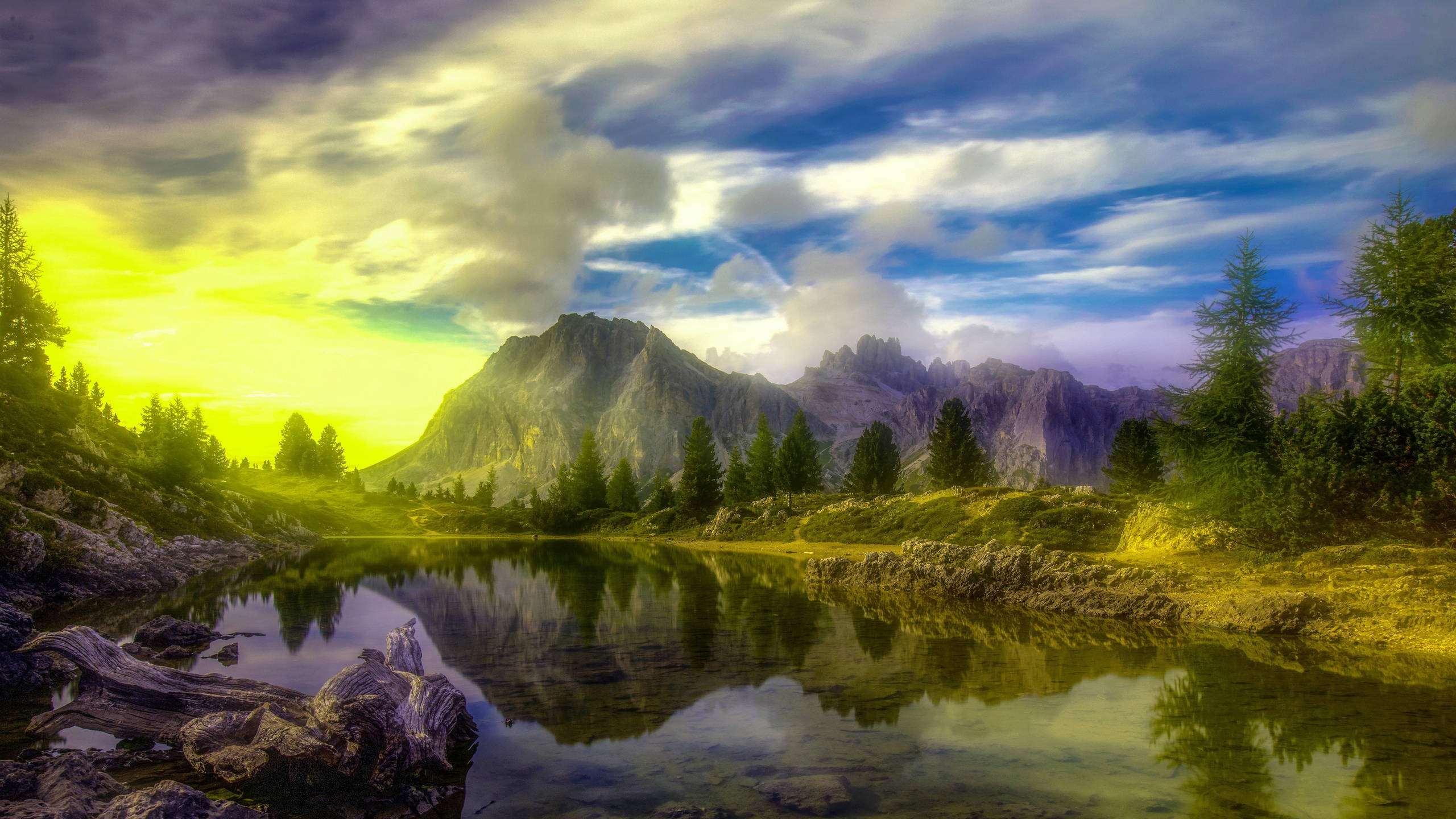 2560x1440 nature 桌布 壁紙 — 寧靜的山間湖泊映照著金色日出雲彩和鋸齒狀山峰，周圍環繞著常青樹。