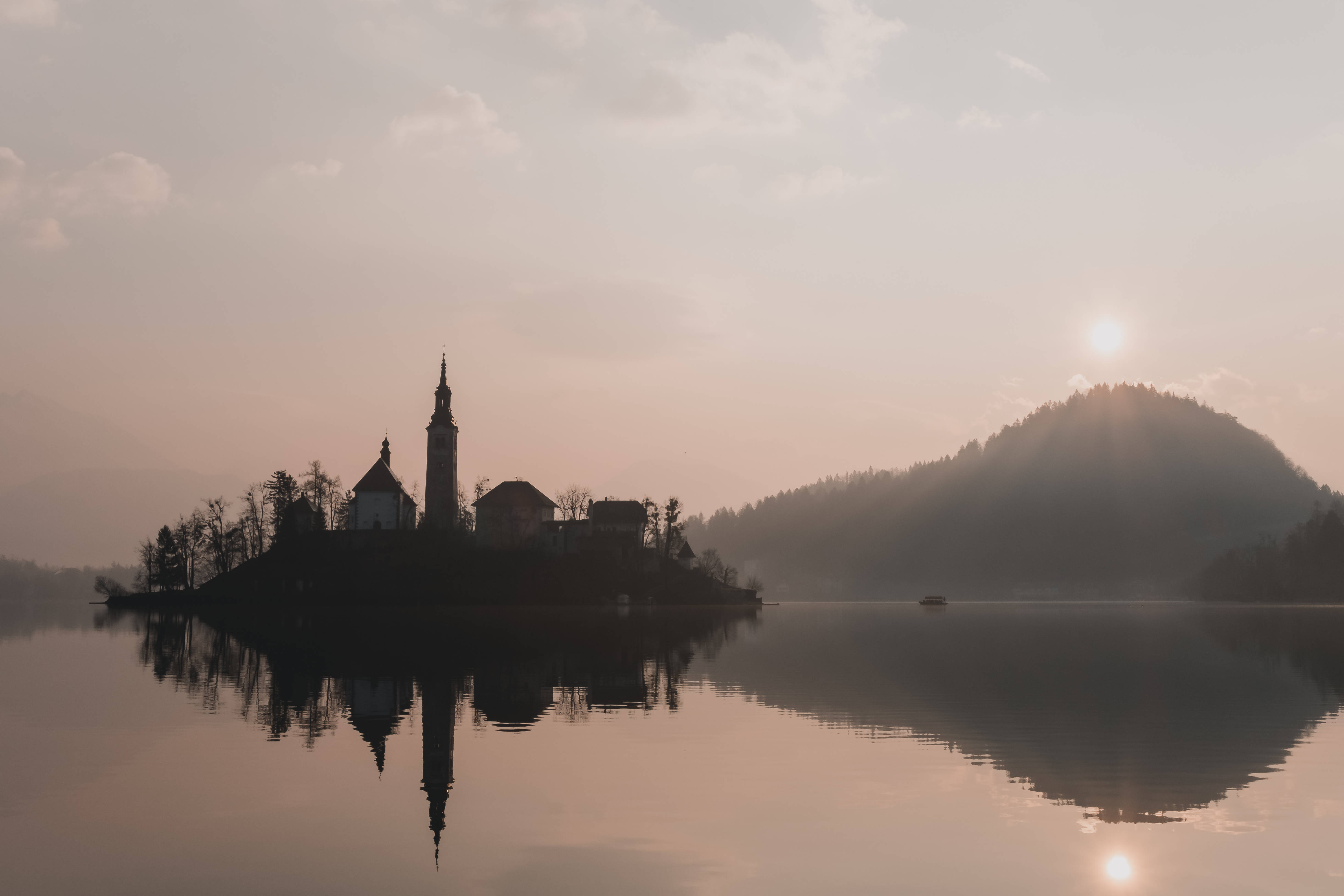 Slovenia 桌布 壁紙 — 寧靜的日出在霧氣瀰漫的湖面上灑下金色光芒，島上的一座教堂完美地倒映在平靜的水面上。