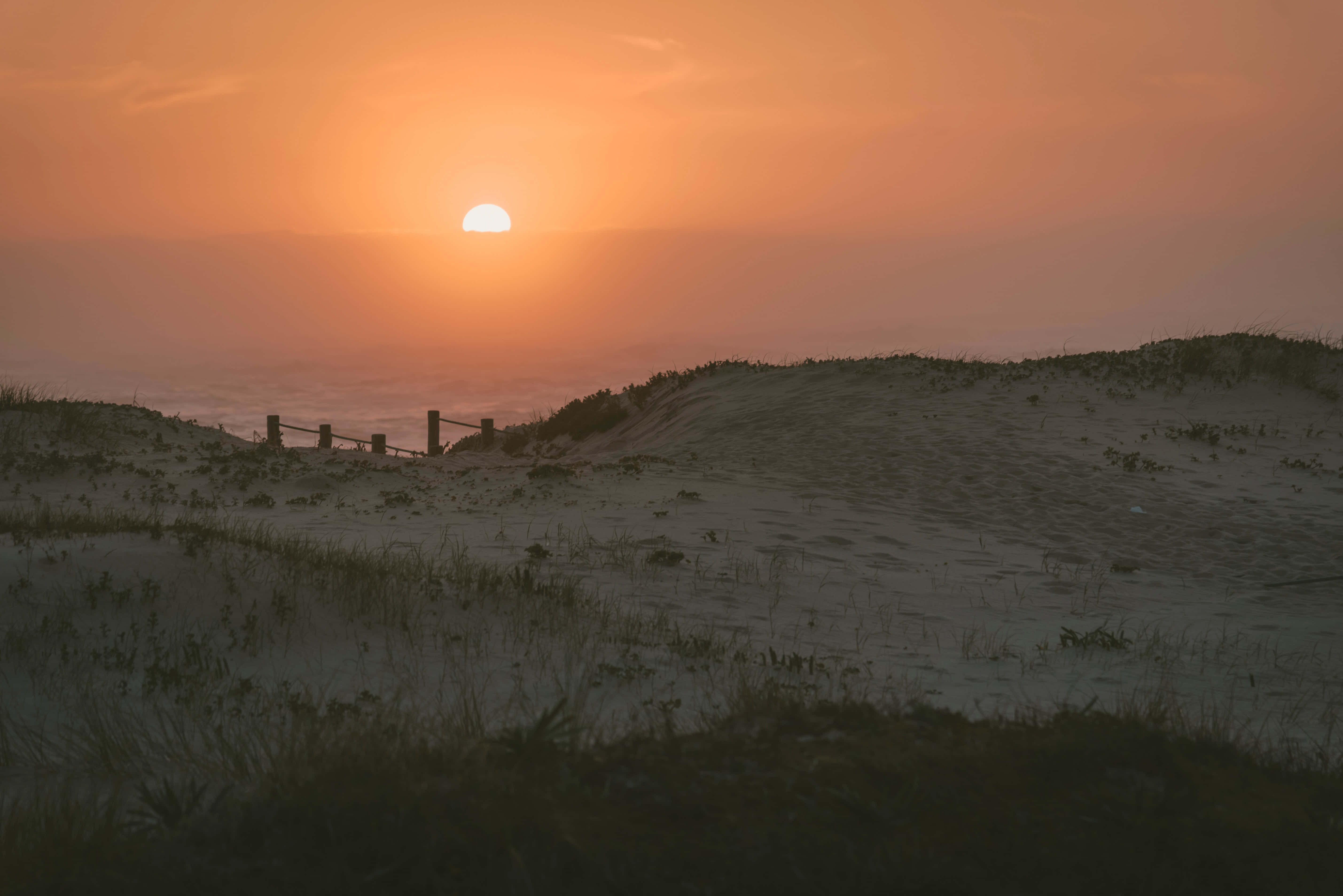 Sunset Beach 桌布 壁紙 — 寧靜的日出照耀著海浪，沙丘和稀疏的草地向地平線延伸。