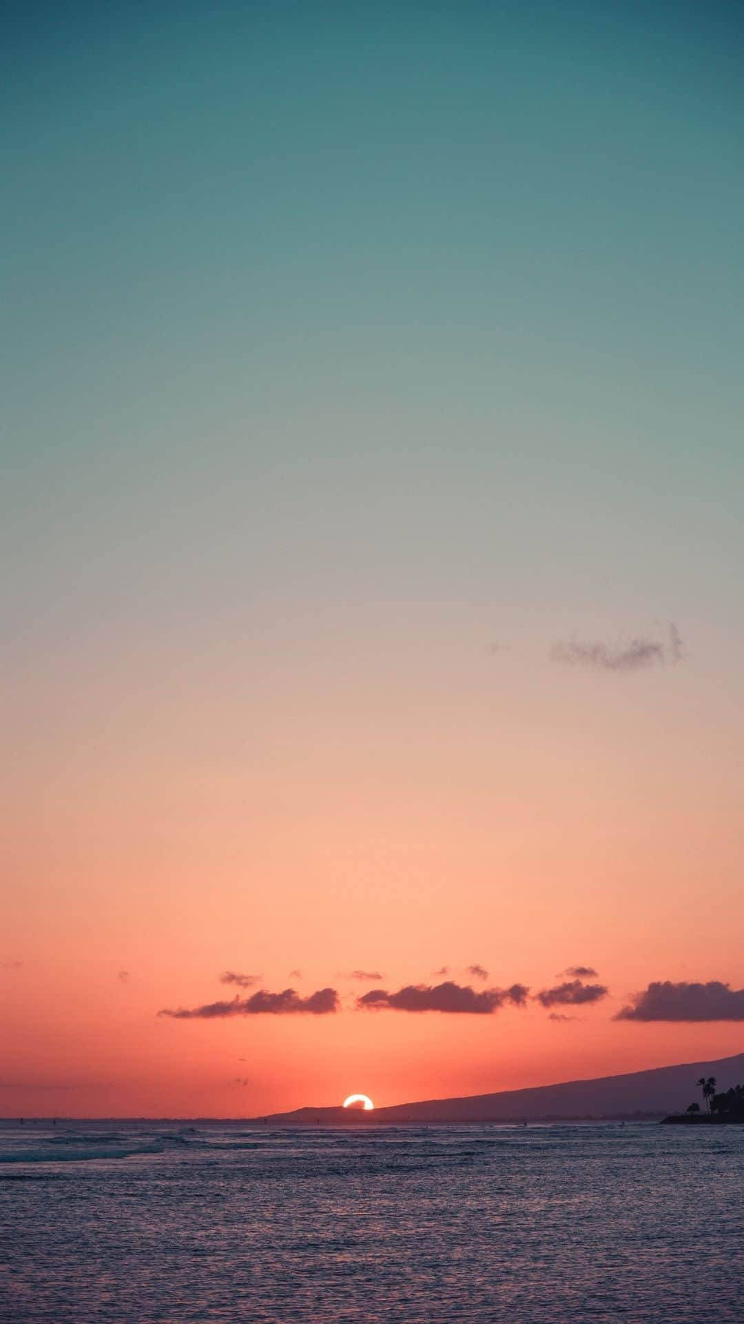 Sunset iPhone 桌布 壁紙 — 寧靜的日落，海面上有發光的太陽沉入遠山脈和散落的雲層之下。