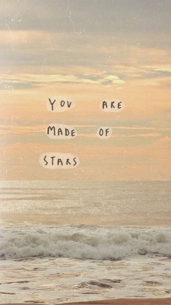 Aesthetic Beige 桌布 壁紙 — 寧靜的日落於海浪之上，天空漂浮著手寫文字 'YOU ARE MADE OF STARS'。