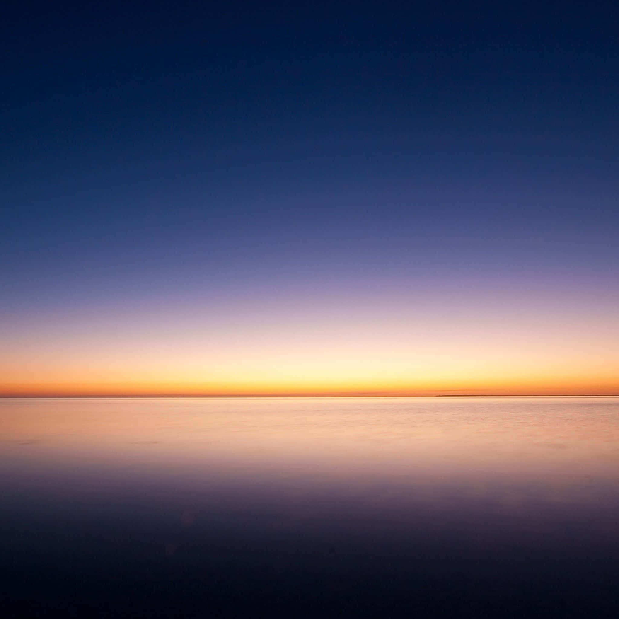 Minimalist Ocean 桌布 壁紙 — 寧靜的暮色天空在平靜的水面上從深藍色過渡到溫暖的橙色。