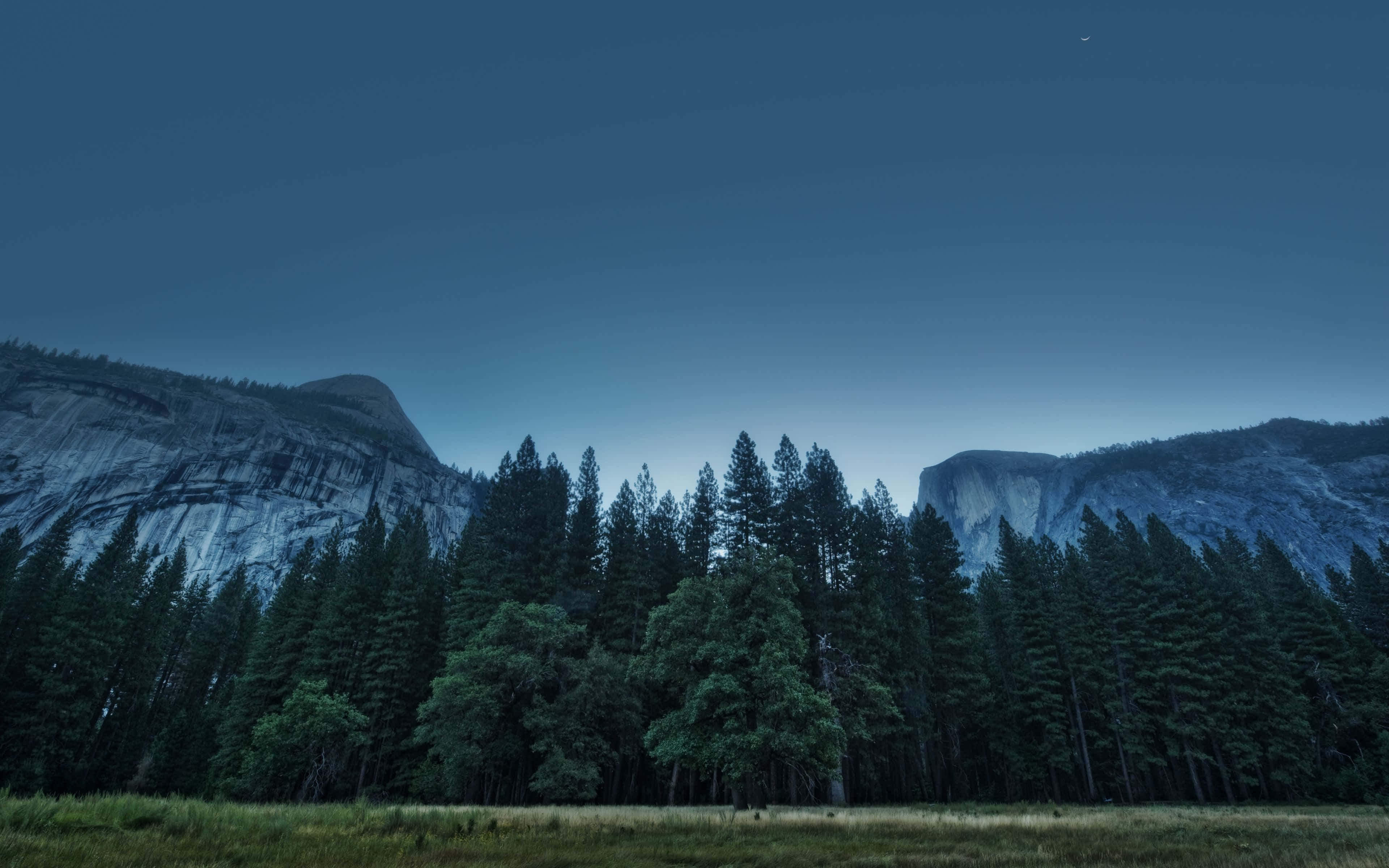 California Mountain 桌布 壁紙 — 寧靜的暮色景觀，高聳的花崗岩懸崖兩旁是茂密的常綠森林，在深藍色的天空下。