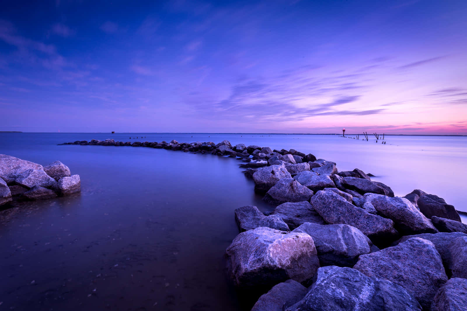 Relaxing Desktop 桌布 壁紙 — 寧靜的暮色海景，平滑的水流過岩石防波堤，天空呈現紫色和粉紅色的漸變。