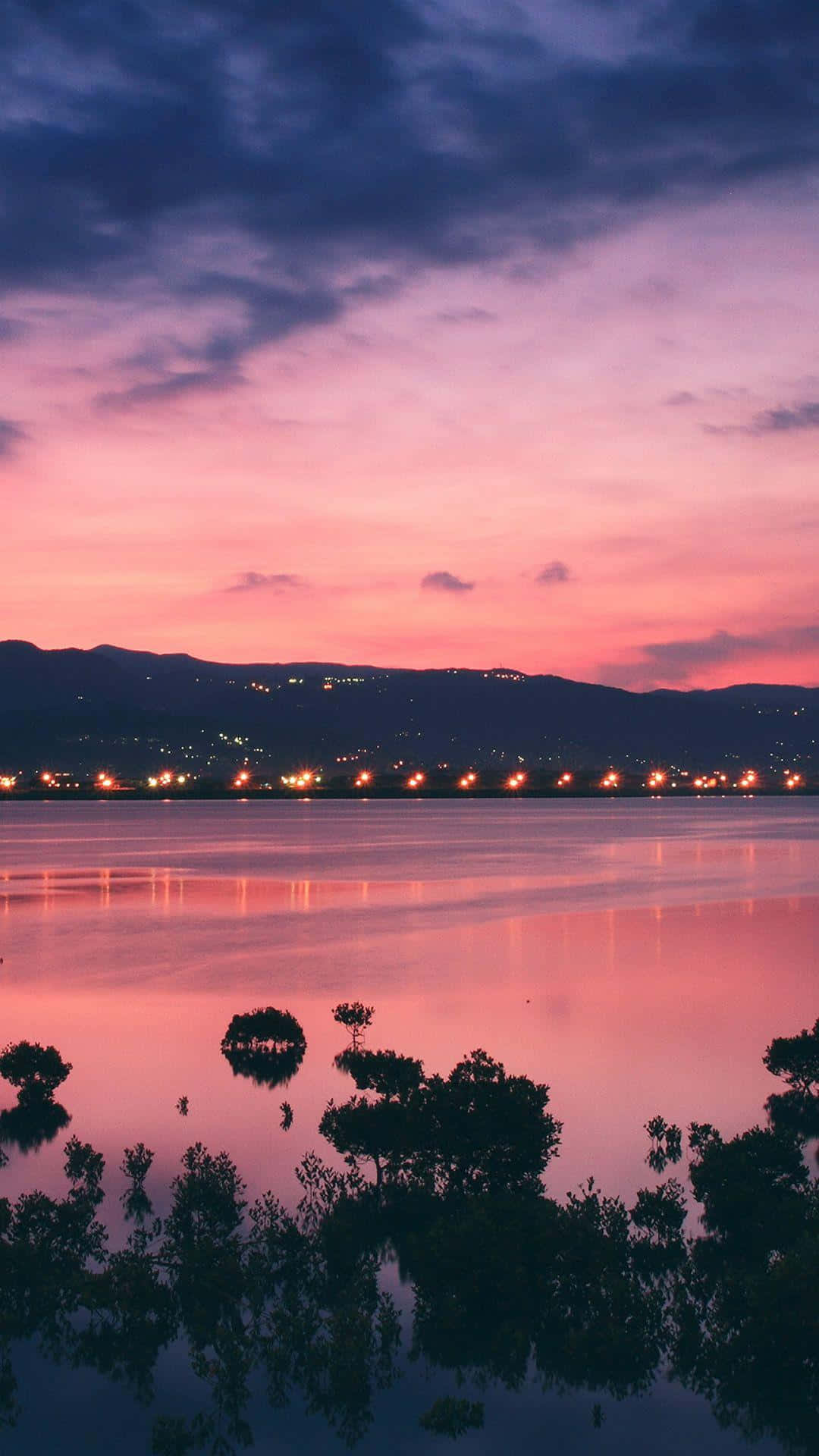 Sunset Landscape 桌布 壁紙 — 寧靜的暮色湖面映照著充滿活力的粉紅和紫色天空，遠方的城市燈光在地平線上閃爍。