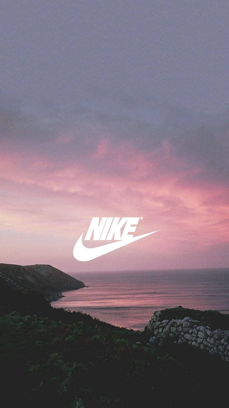 Nike iPhone 桌布 壁紙 — 寧靜的海岸日落，平靜的海面和岩石峭壁上方有粉紅色和紫色的雲彩，並帶有突出的白色Nike標誌。