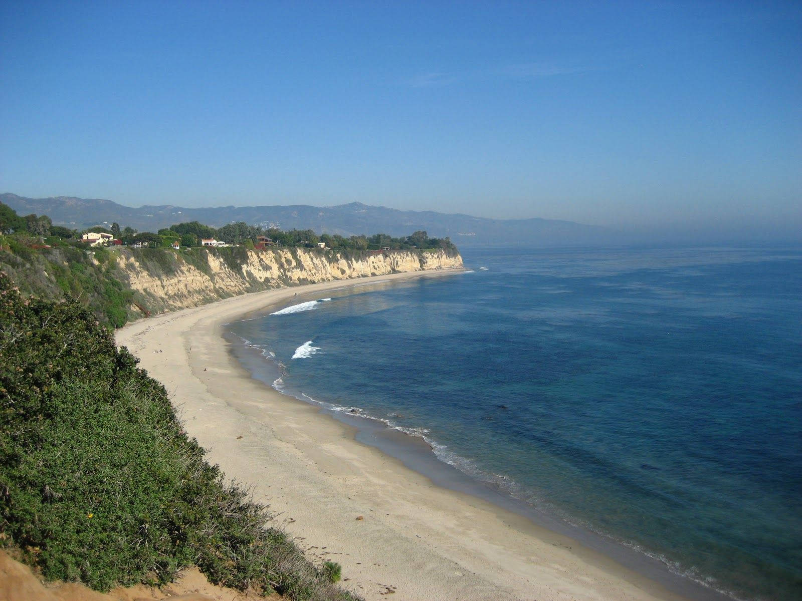 Malibu 桌布 壁紙 — 寧靜的海岸沙灘沿著懸崖蜿蜒，在清澈的藍天下，溫柔的海浪拍打著海岸。