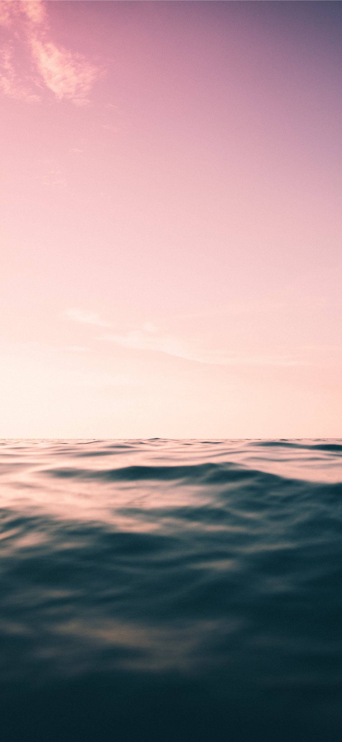 海洋 桌布 壁紙 — 寧靜的海平線沐浴在柔和的粉紅和紫色暮色中，下方是溫柔的波浪。