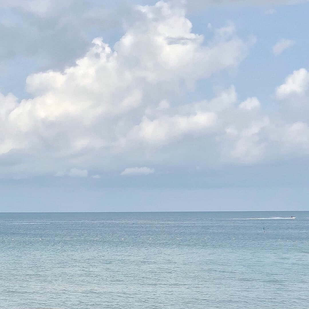 藍色美學 桌布 壁紙 — 寧靜的海洋在廣闊的天空下延伸，天空佈滿蓬鬆的白雲，一艘小船在平靜的碧綠海水上留下一道航跡。