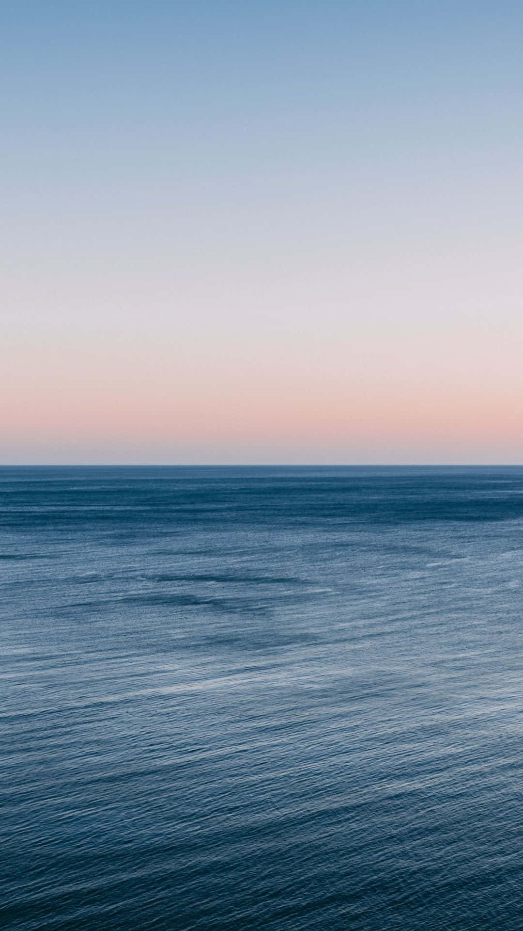 Ocean Aesthetic Phone 桌布 壁紙 — 寧靜的海洋在柔和的粉紅色和藍色暮色天空下延伸至地平線。