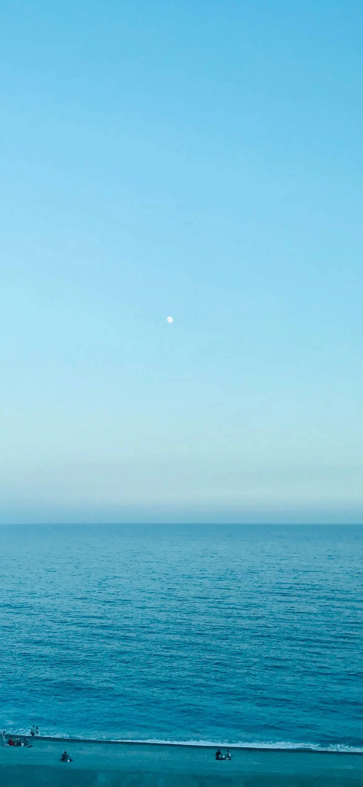 iPhone 桌布 壁紙 — 寧靜的海洋延伸到地平線，天空清澈湛藍，一輪明亮的月亮清晰可見。