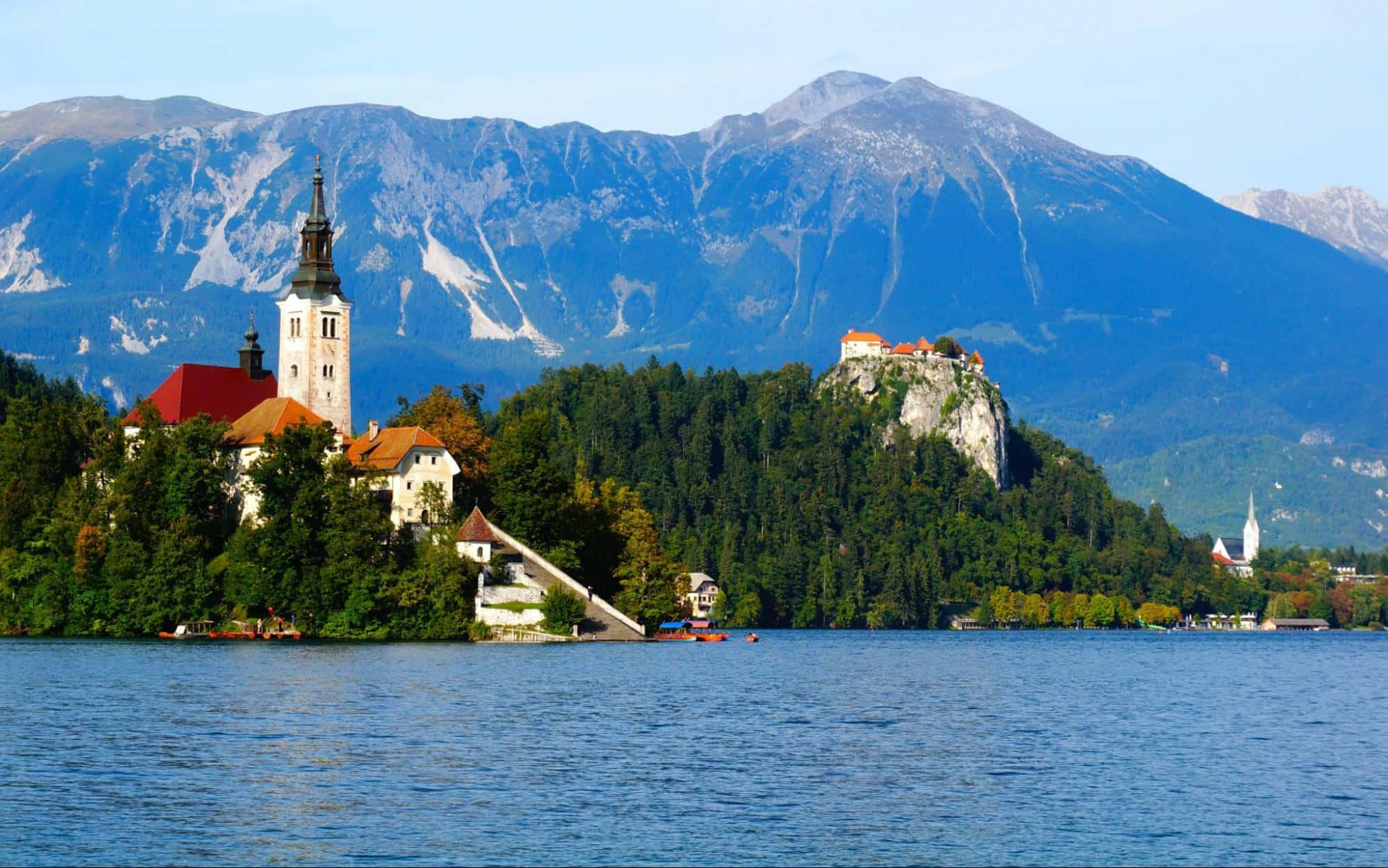 Lake Bled 桌布 壁紙 — 寧靜的湖景，歷史悠久的教堂坐落於鬱鬱蔥蔥的島嶼上，城堡矗立在懸崖上，背後是高聳的山脈。