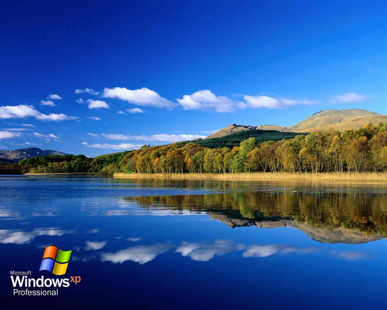 Windows XP 桌布 壁紙 — 寧靜的湖面映照著明亮的藍天、蓬鬆的白雲，以及沐浴在燦爛陽光下秋色斑斕的樹林山丘。
