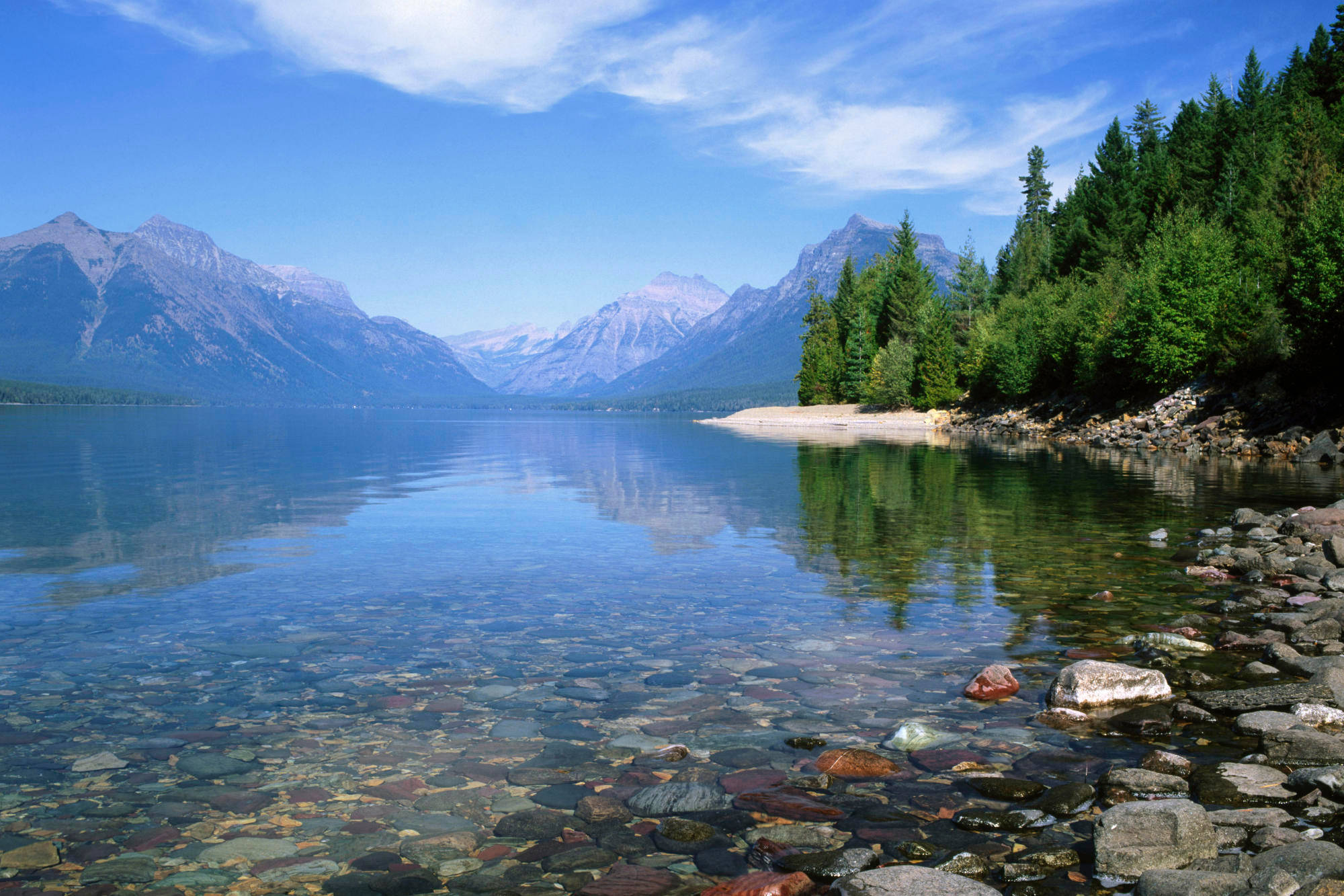 Montana 桌布 壁紙 — 寧靜的湖面映照著積雪的山峰和常綠樹，天空湛藍，白雲輕柔。