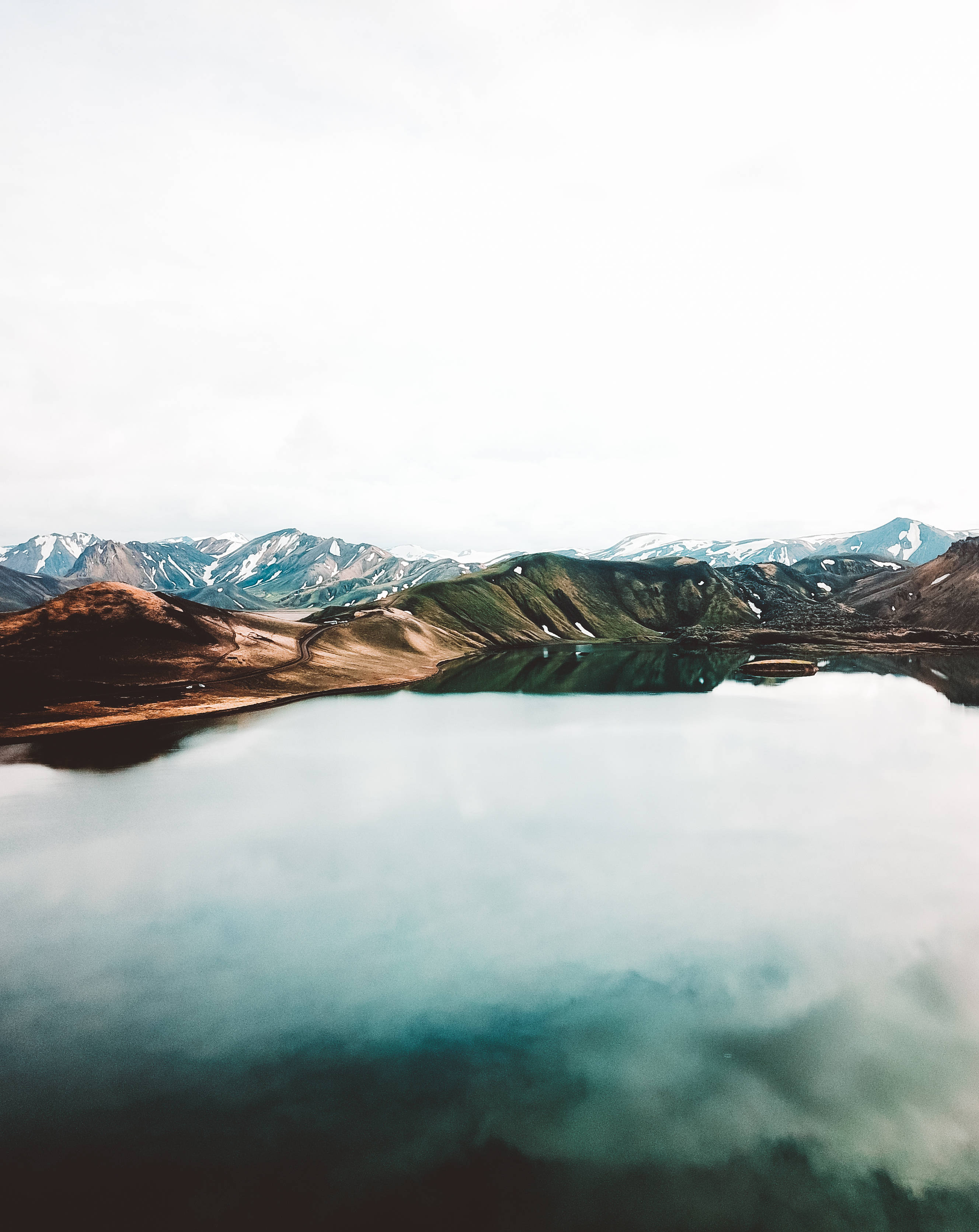 自然風景動圖 桌布 壁紙 — 寧靜的湖面映照著陰天下的雪山，前景是土色的丘陵。