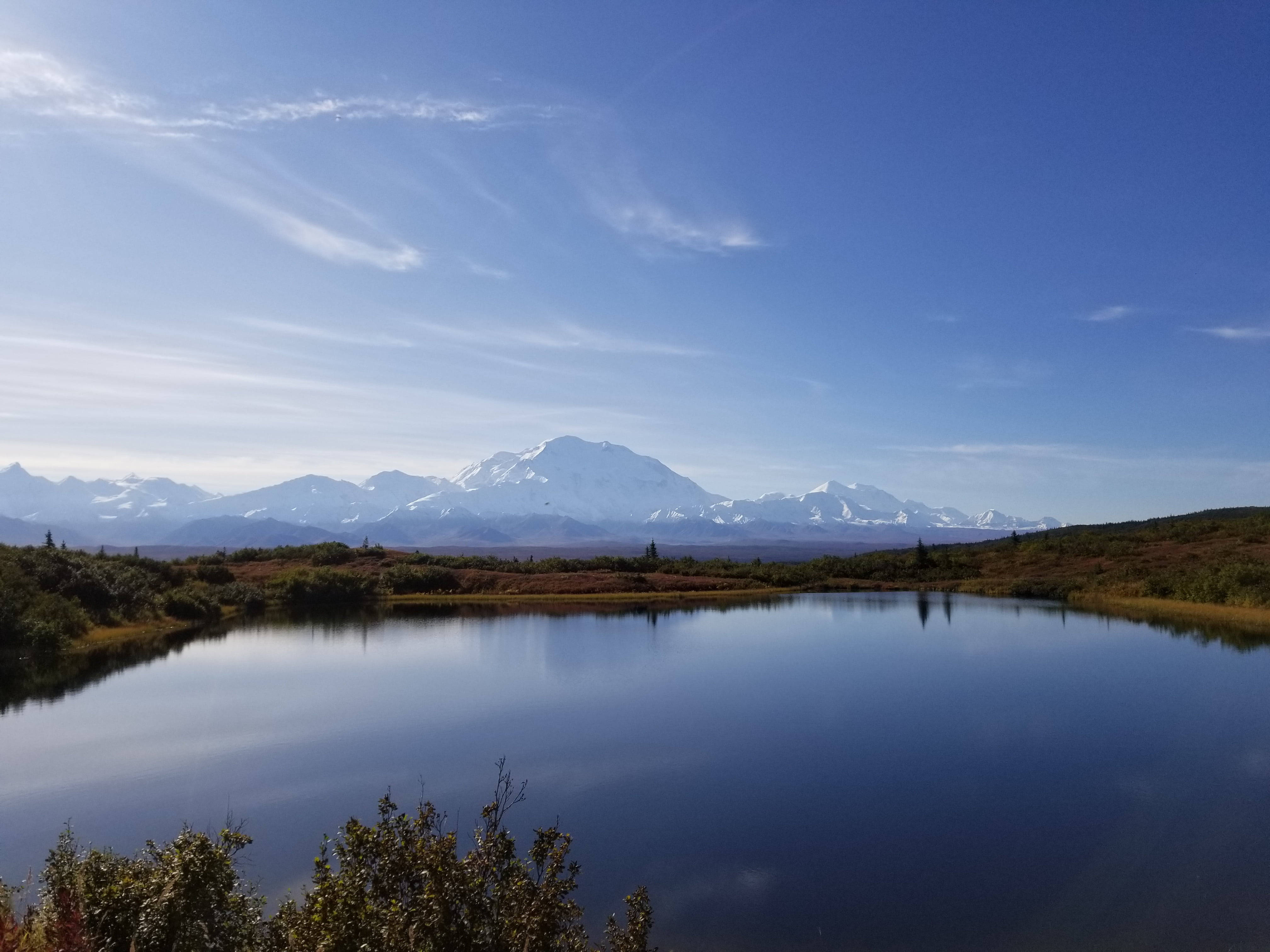 Lake 桌布 壁紙 — 寧靜的湖面映照著雄偉的雪山德納利山脈，天空湛藍，雲彩輕柔。
