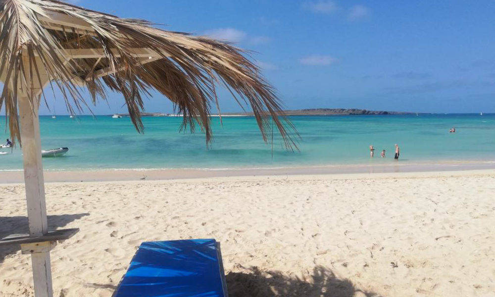 Vacation 桌布 壁紙 — 寧靜的熱帶海灘，碧綠的海水，一把茅草傘在藍色躺椅上投下陰影。