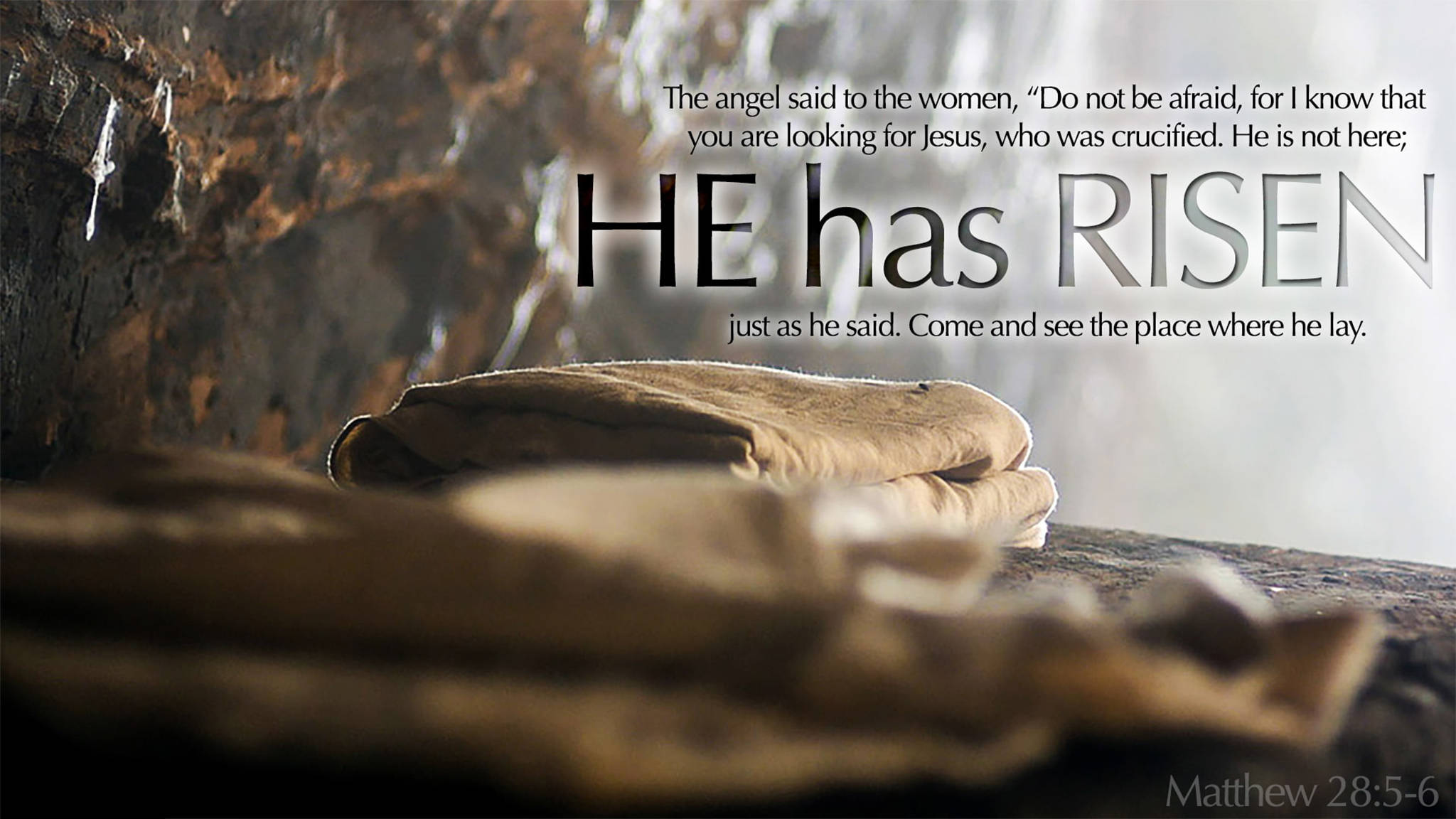 Bible Quotes 桌布 壁紙 — 寧靜的石墓，內有摺疊的裹屍布，並在柔和晨光中宣告『祂已復活』的文字。