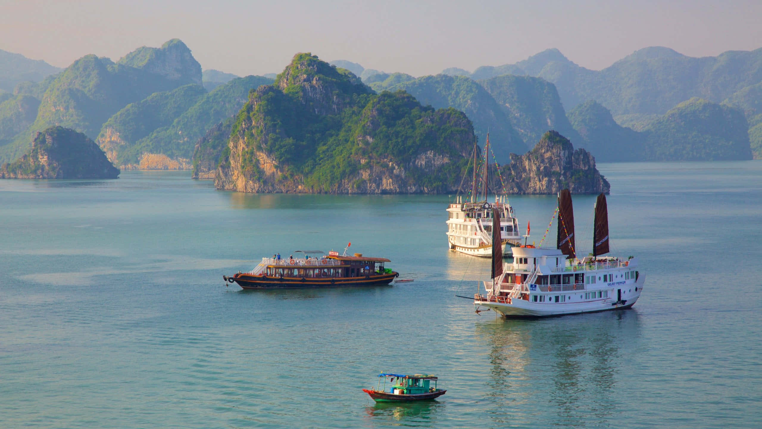 Vietnam 桌布 壁紙 — 寧靜的碧綠海水環抱著鬱鬱蔥蔥的綠色喀斯特島嶼，傳統船隻在平靜的海灣中輕輕漂浮。