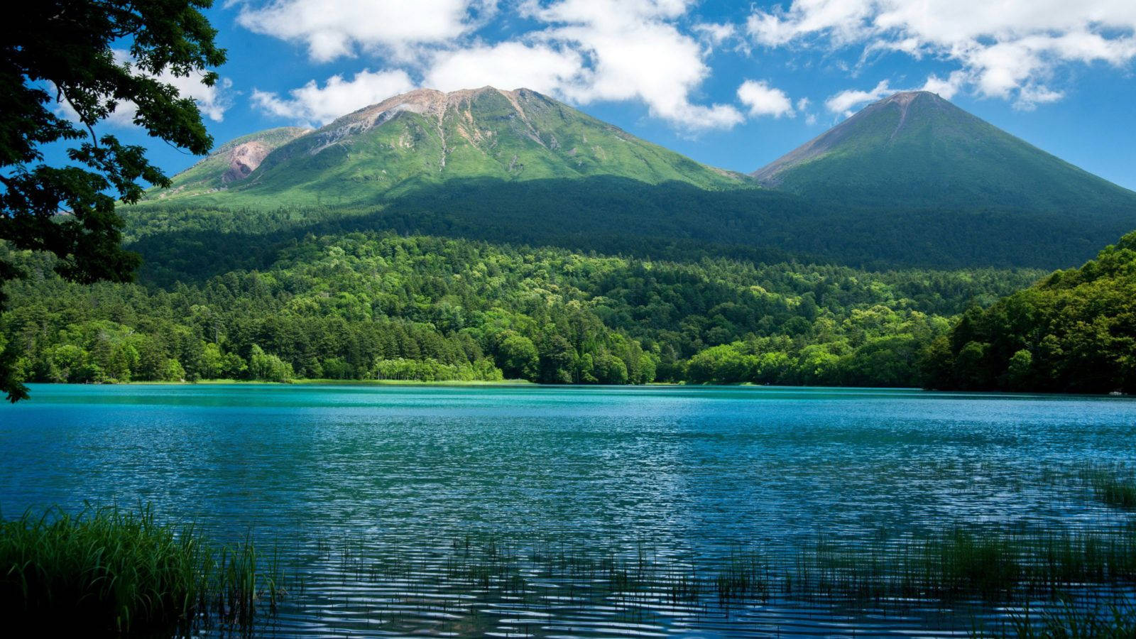 自然 桌布 壁紙 — 寧靜的碧綠湖泊映照著兩座鬱鬱蔥蔥的青山，上方是明亮的藍天和蓬鬆的白雲。