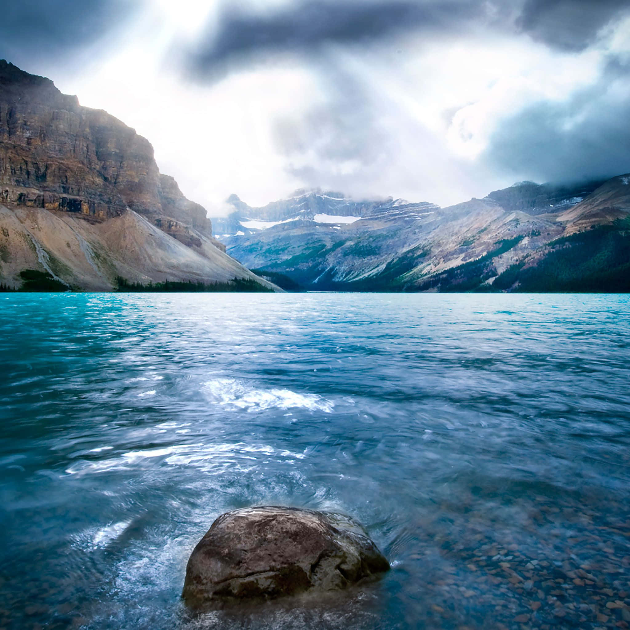 Lake View 桌布 壁紙 — 寧靜的碧綠湖面倒映著暴風雨的天空，背景中崎嶇的山脈聳立，山頂覆蓋著白雪。