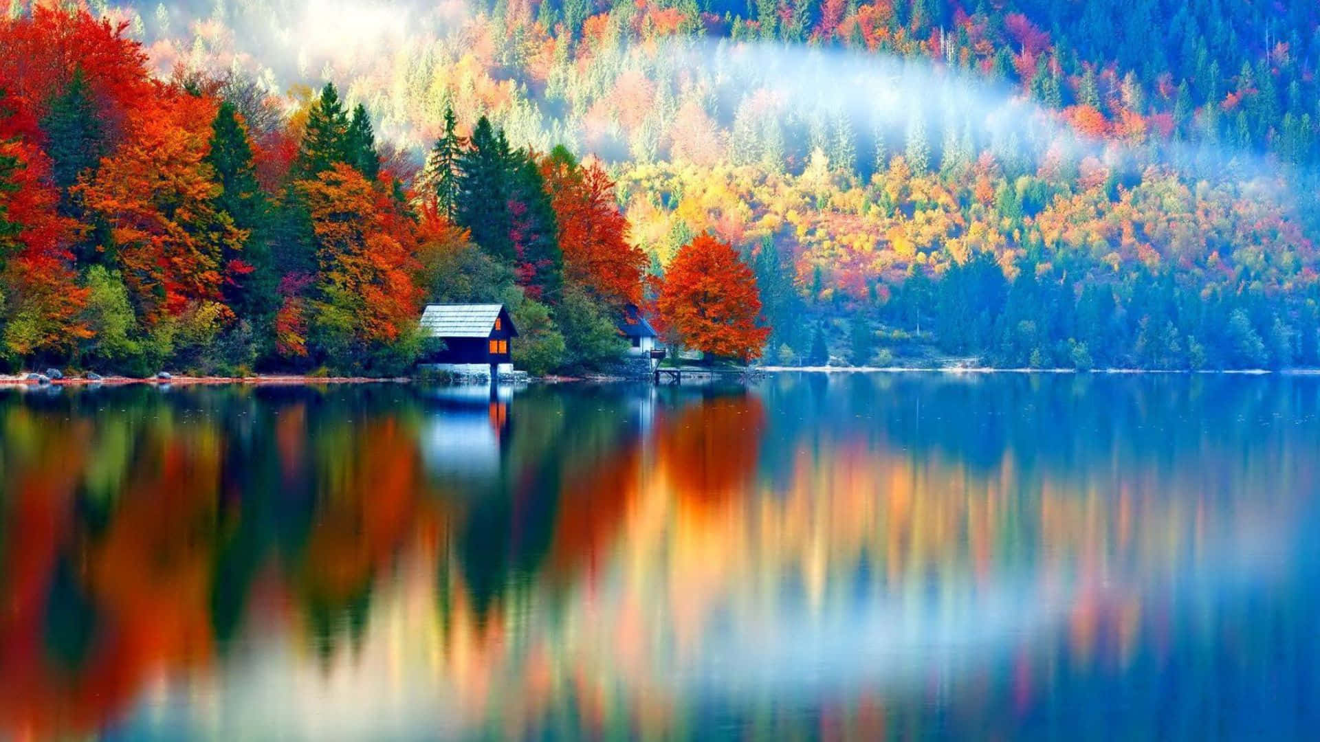 Fall Lake 桌布 壁紙 — 寧靜的秋日湖泊倒映著火紅、橙黃和金黃的樹木，薄霧在森林覆蓋的山丘上繚繞。