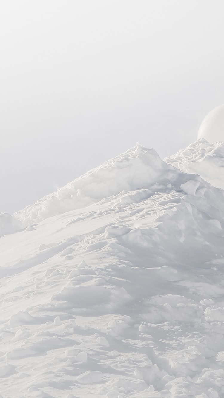 桌布 壁紙 — 寧靜的雪山頂在蒼白的天空下，透過柔和的薄霧升起，帶有微弱的太陽光暈。