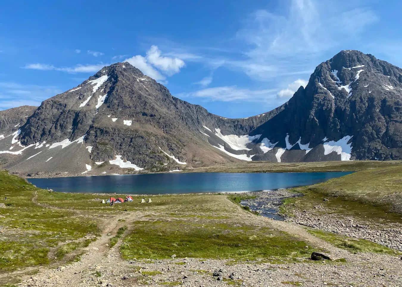 Mountain Scenery 桌布 壁紙 — 寧靜的高山湖泊，坐落於積雪的山峰之間，草地上有一個小露營地，上方是清澈的藍天。