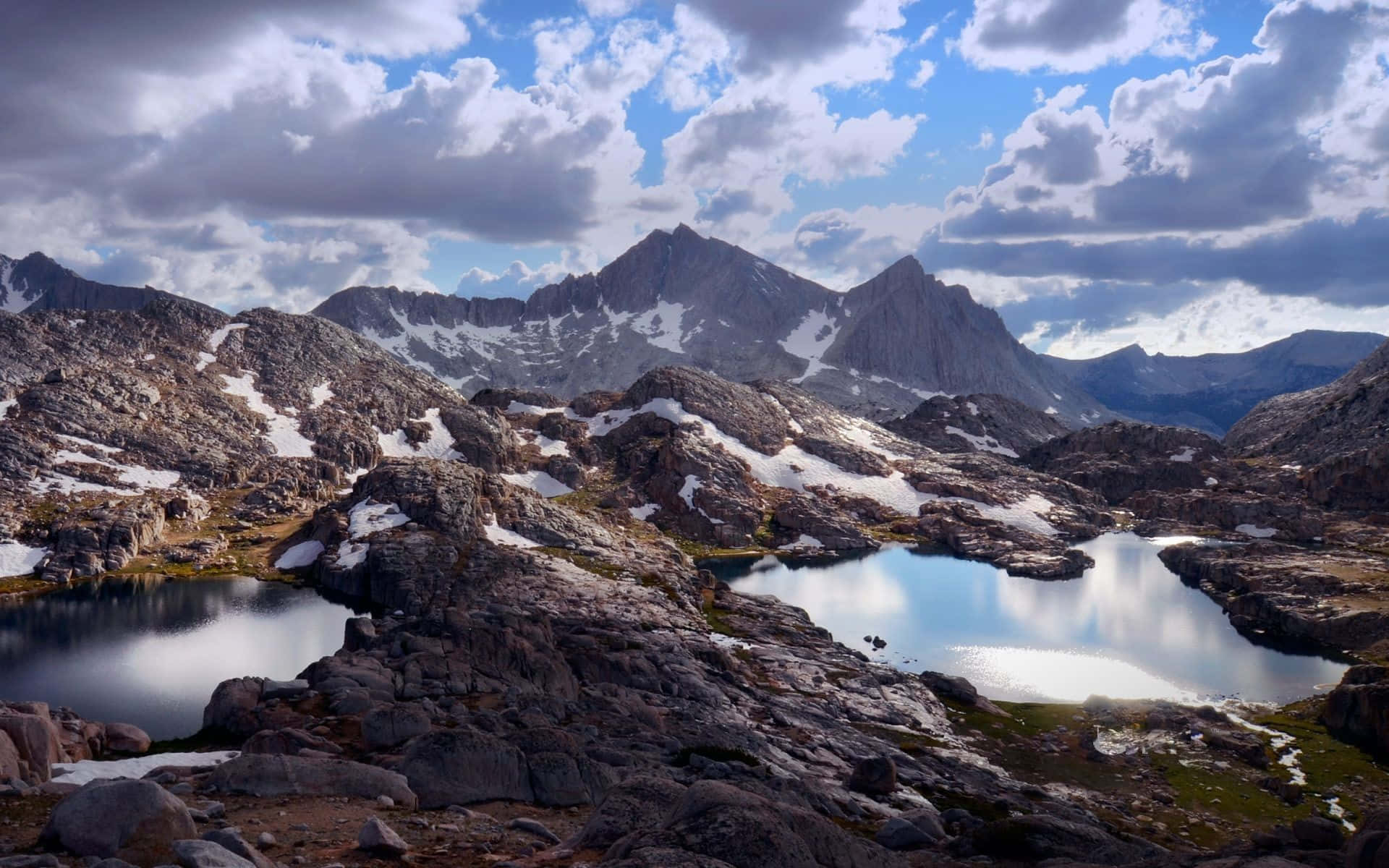 High Sierra 桌布 壁紙 — 寧靜的高山湖泊映照著戲劇性的天空，上方是鋸齒狀、覆蓋著白雪的山峰和岩石地形。
