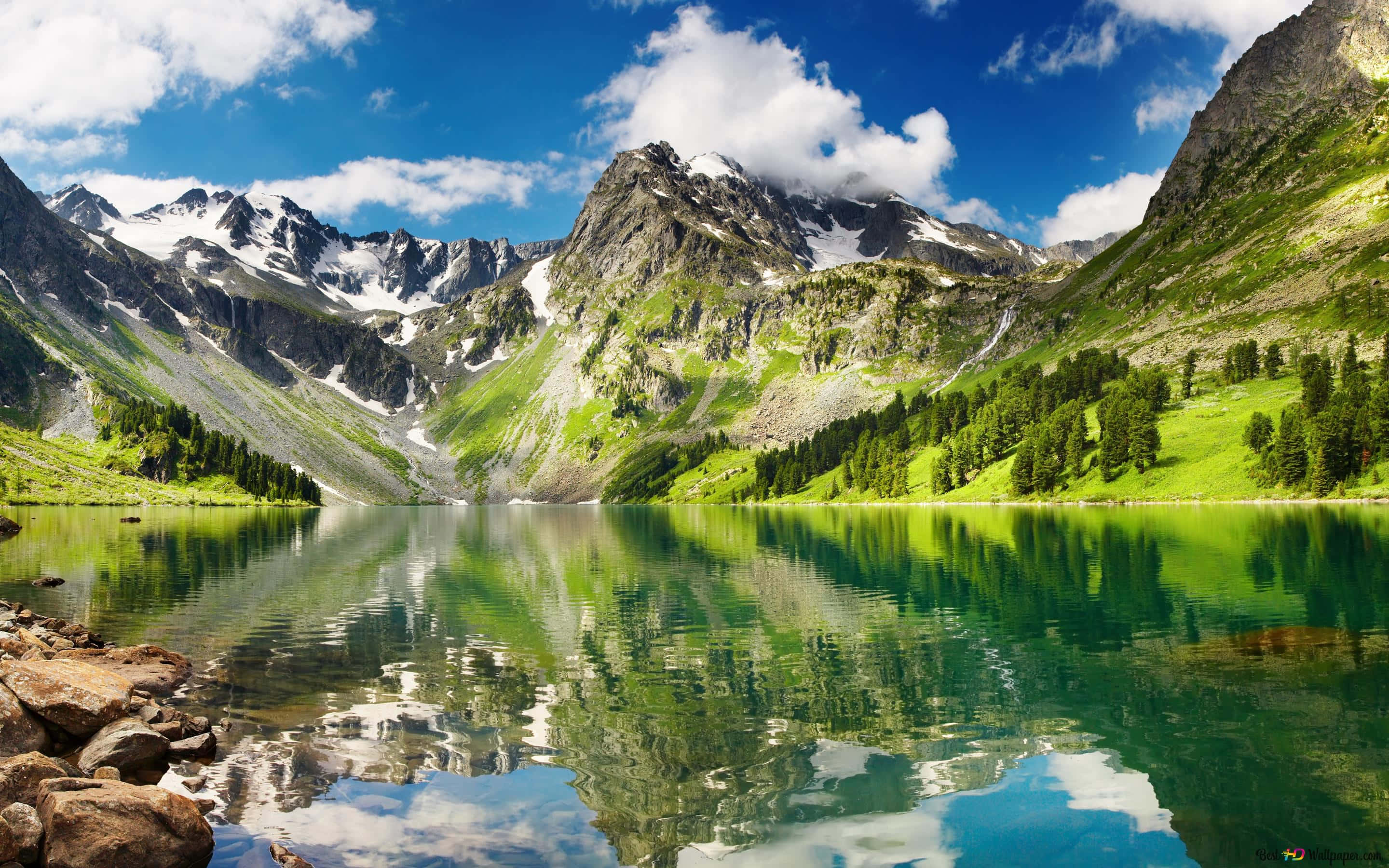Beautiful Mountain Lake 桌布 壁紙 — 寧靜的高山湖泊映照著白雪覆蓋的山峰和翠綠的山坡，天空湛藍，白雲朵朵。