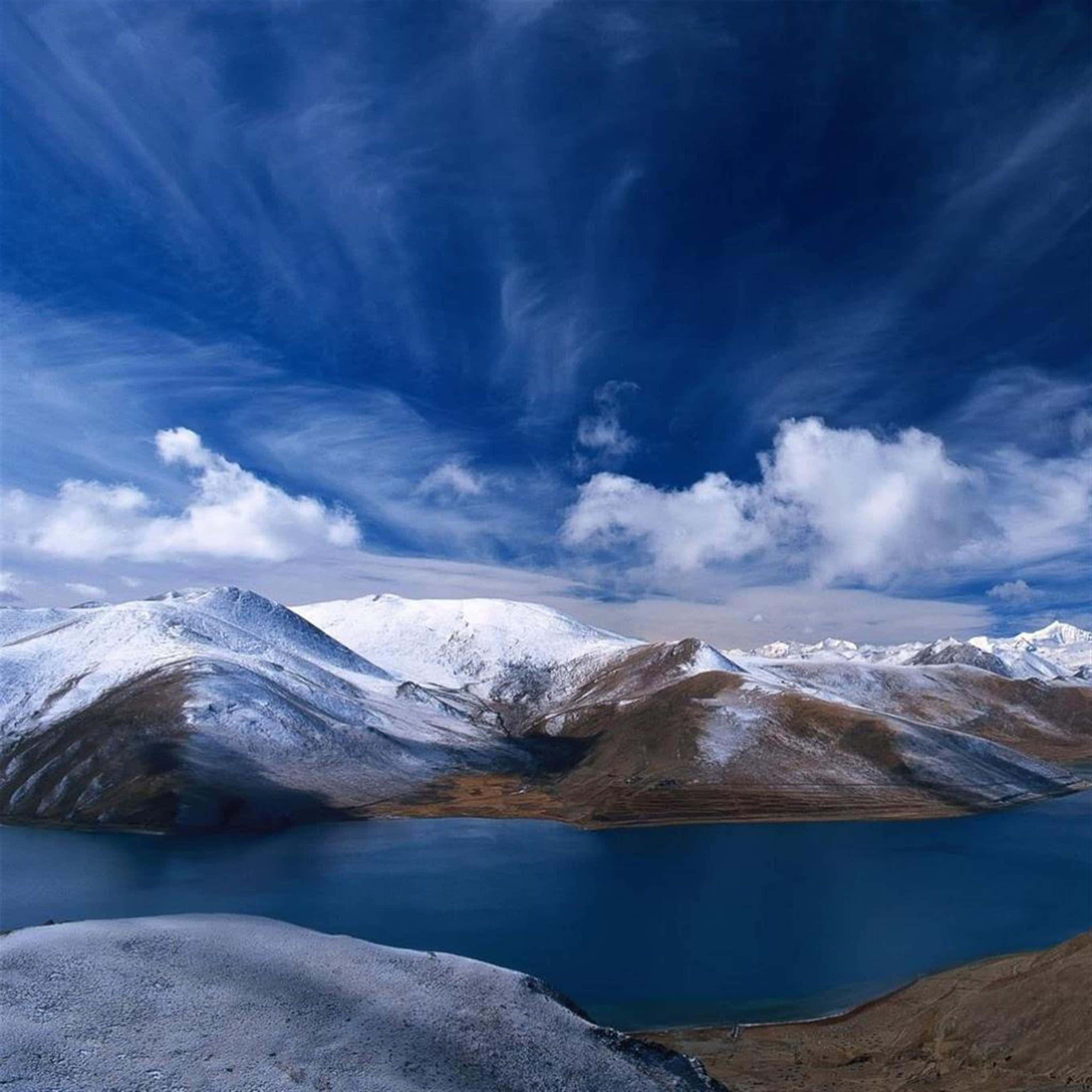 iPad Pro 桌布 壁紙 — 寧靜的高山湖泊映照著白雪覆蓋的山峰，廣闊的藍天點綴著縷縷薄雲。