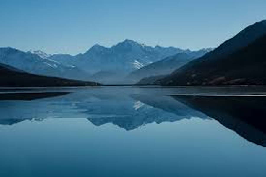 桌布 壁紙 — 寧靜的高山湖泊映照著白雪覆蓋的山峰，天空湛藍，山谷霧氣繚繞。
