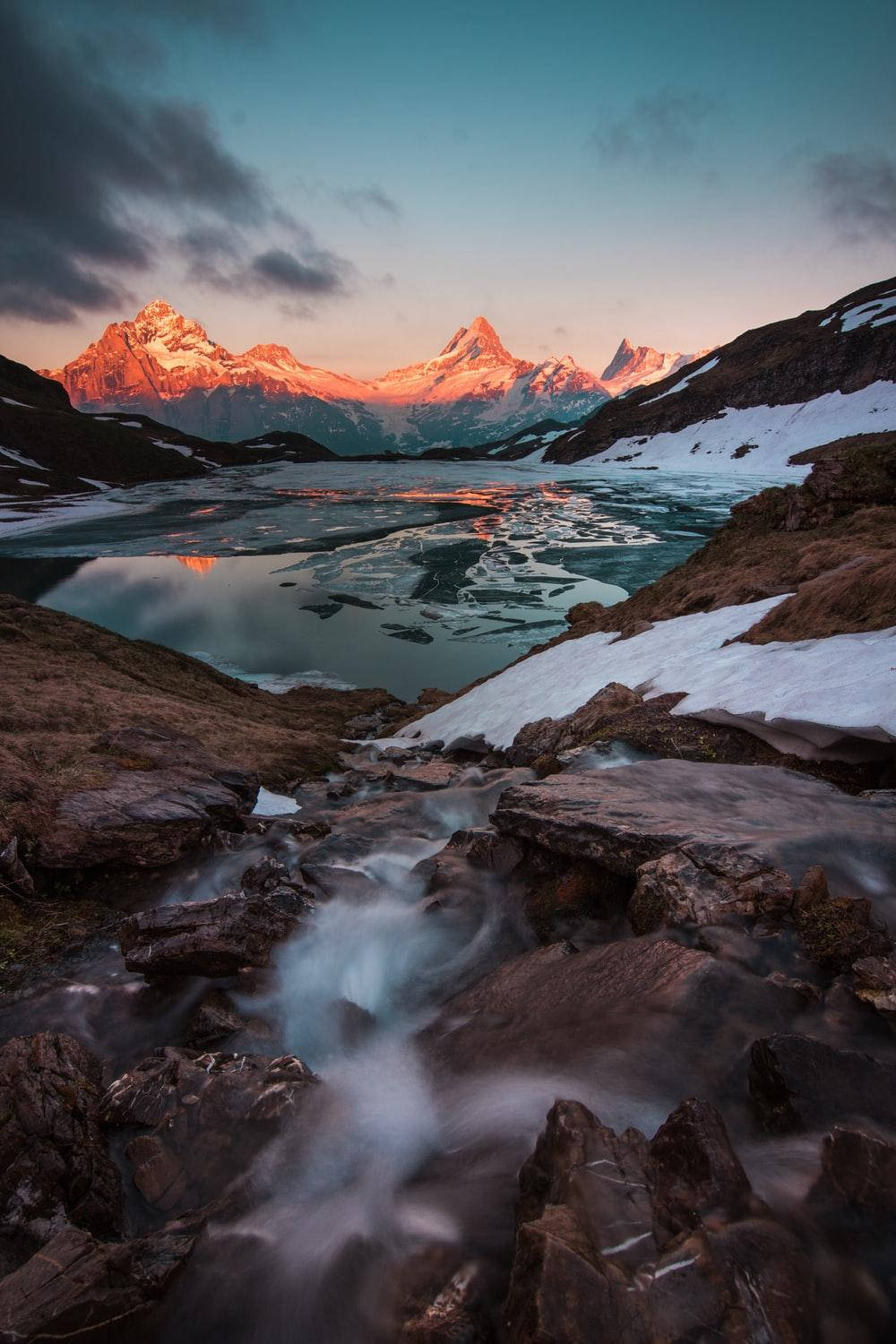 山脈 桌布 壁紙 — 寧靜的高山湖泊映照著被白雪覆蓋的山峰，在夕陽餘暉中閃耀，冰塊碎片在平靜的水面上漂流。