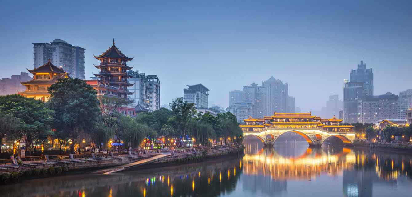 Chengdu 桌布 壁紙 — 寧靜的黃昏城市景觀，一座發光的傳統橋樑橫跨平靜的河流，背景是現代摩天大樓和寶塔式建築。