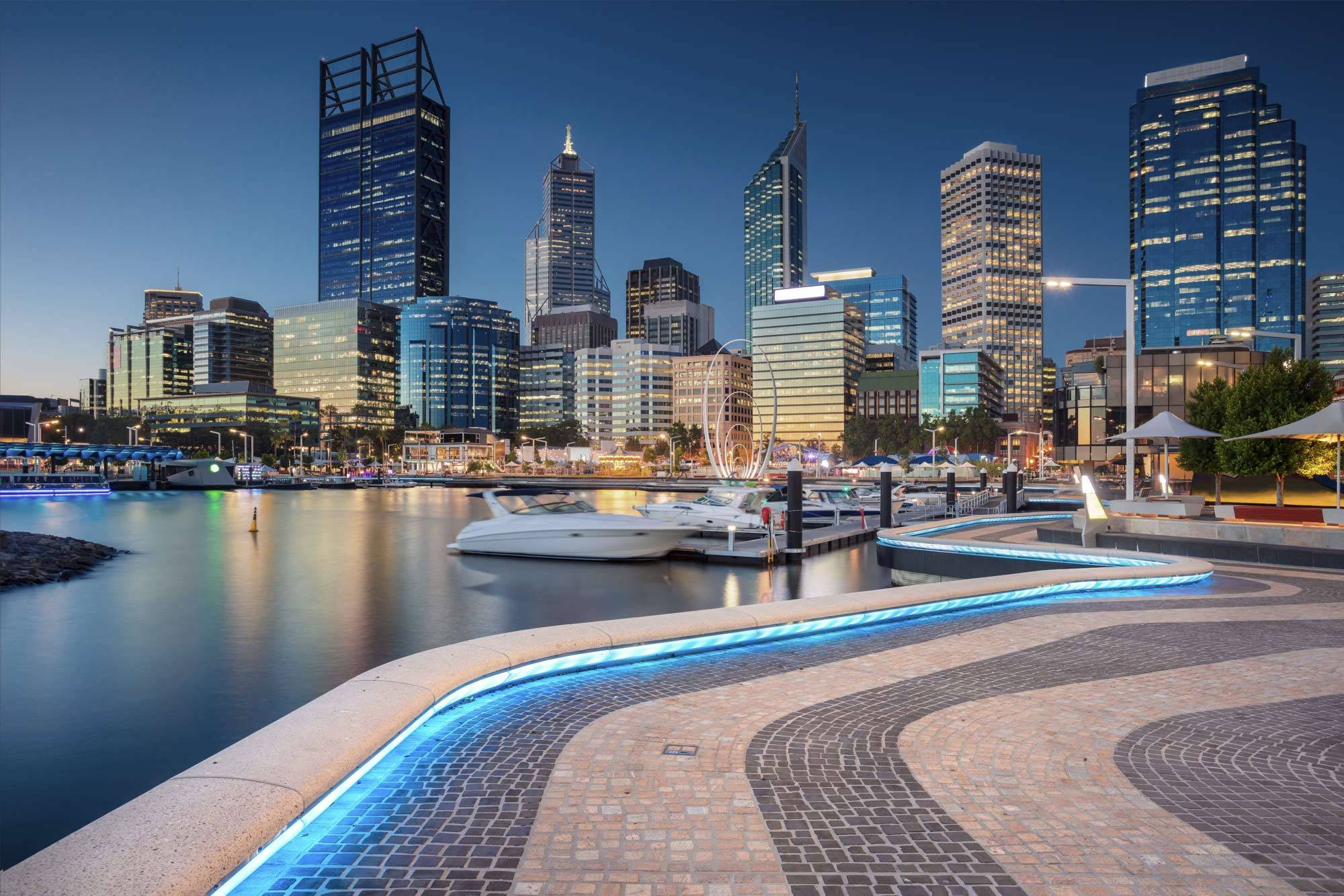 Perth 桌布 壁紙 — 寧靜的黃昏城市景觀，發光的摩天大樓倒映在平靜的水面上，旁邊是彎曲的照明步道。