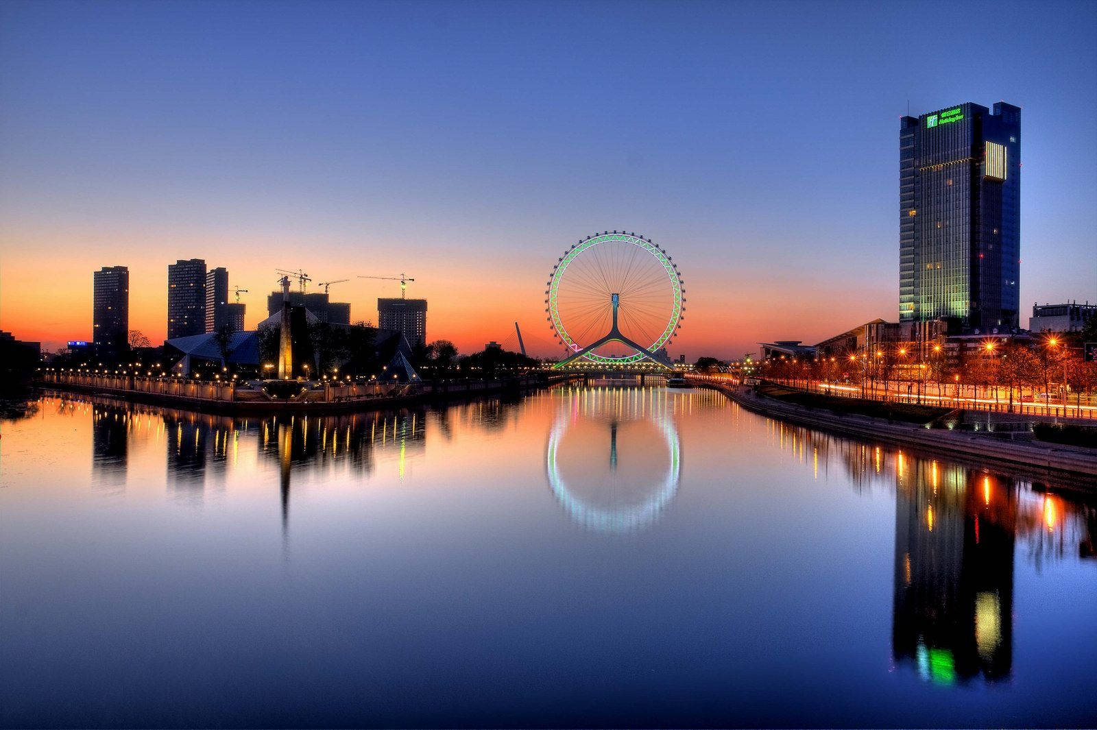 Tianjin 桌布 壁紙 — 寧靜的黃昏城市景觀，發光的摩天輪和摩天大樓倒映在平靜的水面上。
