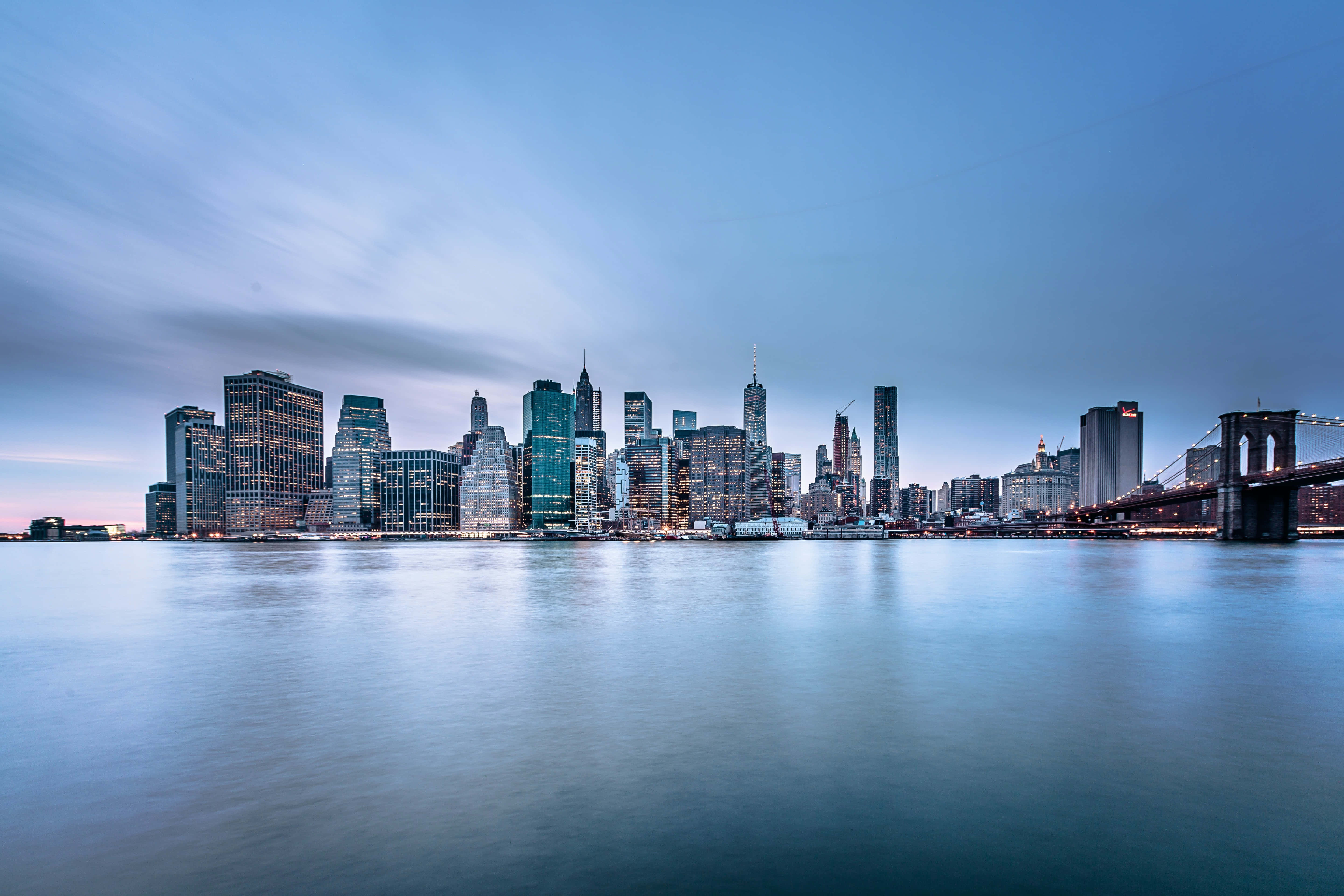 Nyc 桌布 壁紙 — 寧靜的黃昏景色，紐約市天際線與布魯克林大橋倒映在平靜的水面上。