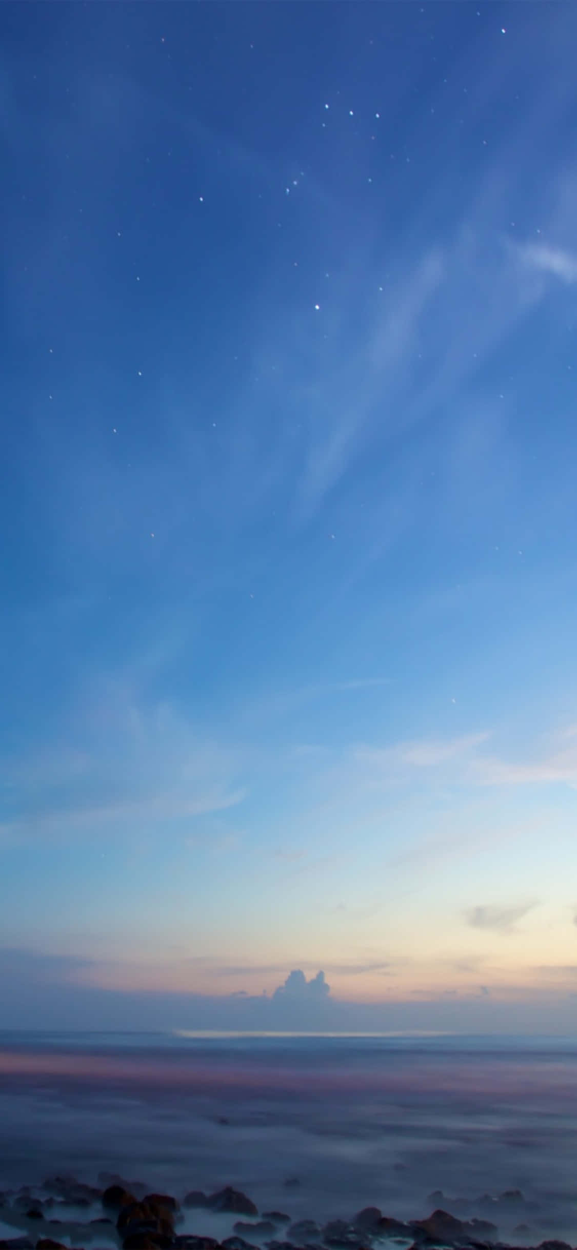 iPhone X Beach 桌布 壁紙 — 寧靜的黃昏海景，星星在漸變色的天空中浮現，映照在平靜的水面和深色岩石之上。