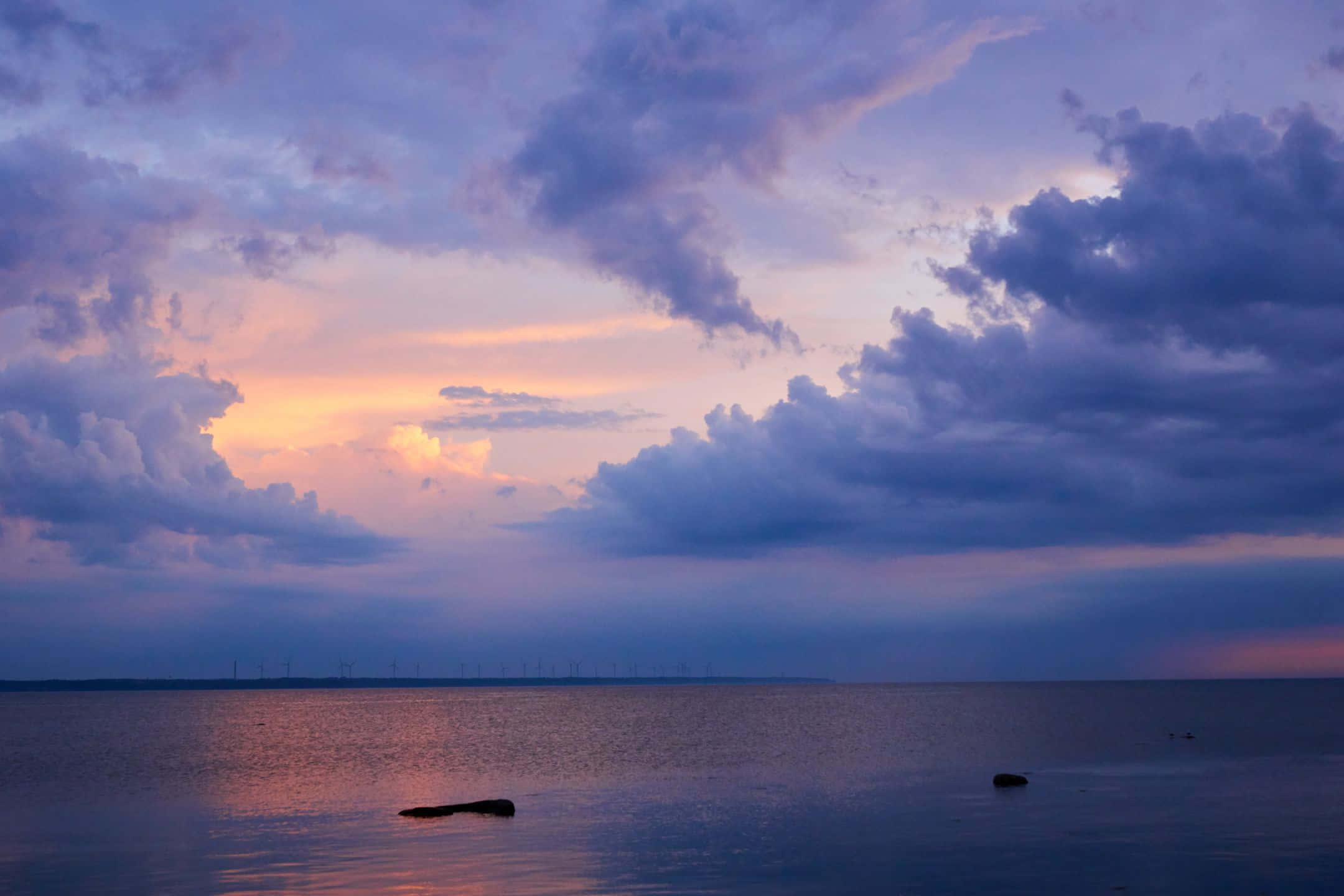 2160x1440 桌布 壁紙 — 寧靜的黃昏海景，紫色和橙色的雲彩映照在平靜的水面上，遠方地平線上有風力發電機。