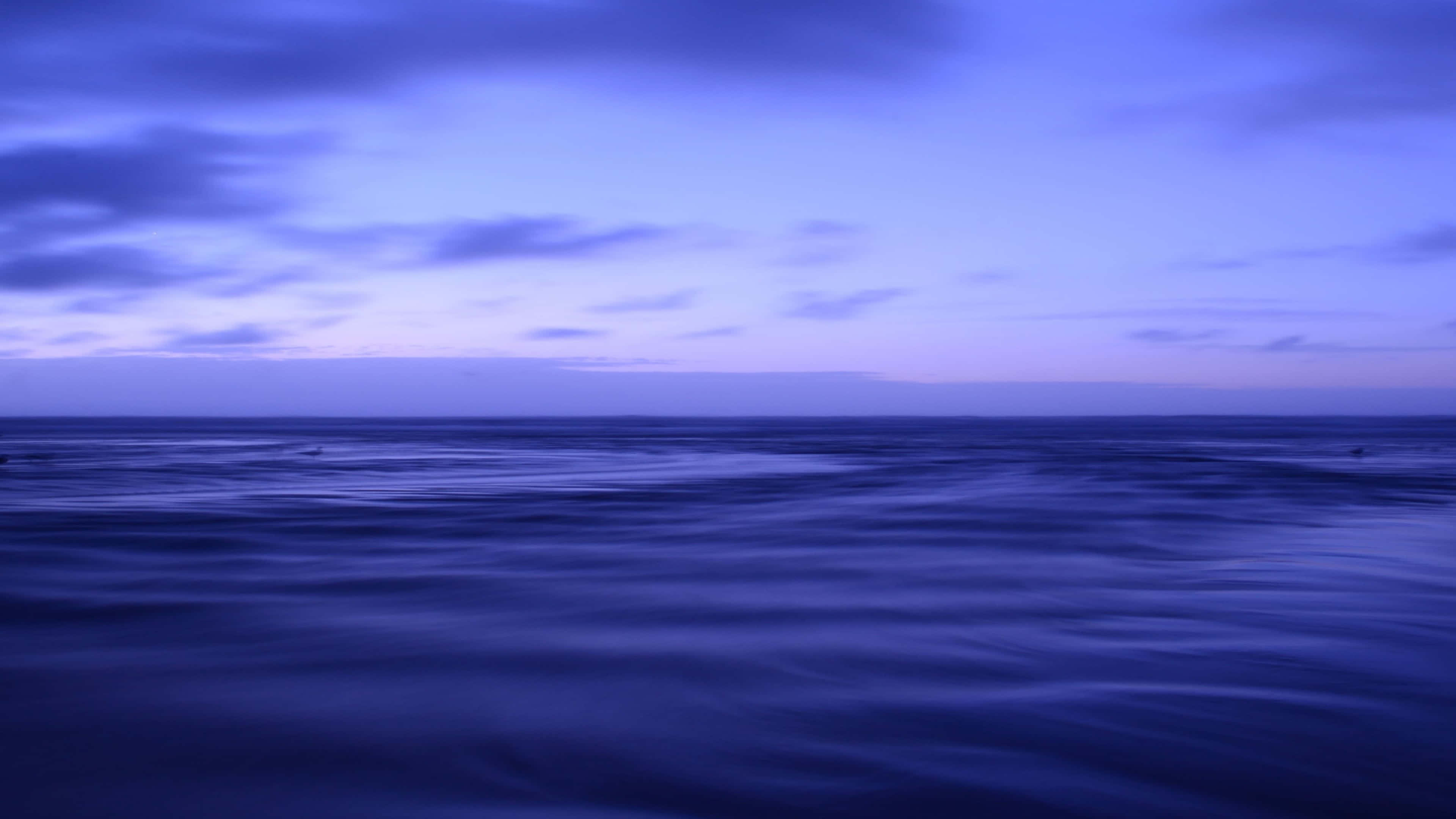 海景 桌布 壁紙 — 寧靜的黃昏海洋，平滑的藍色波浪在柔和的紫色天空下，散佈著雲朵。