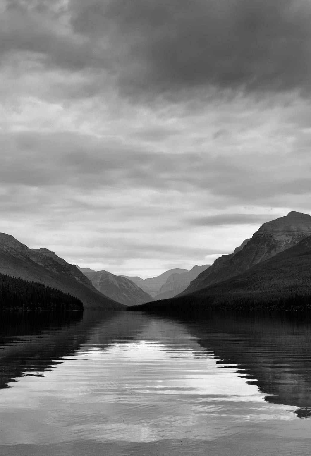 Black And White iPhone 桌布 壁紙 — 寧靜的黑白湖泊映照出高聳的山脈，天空烏雲密佈，氣氛戲劇化。