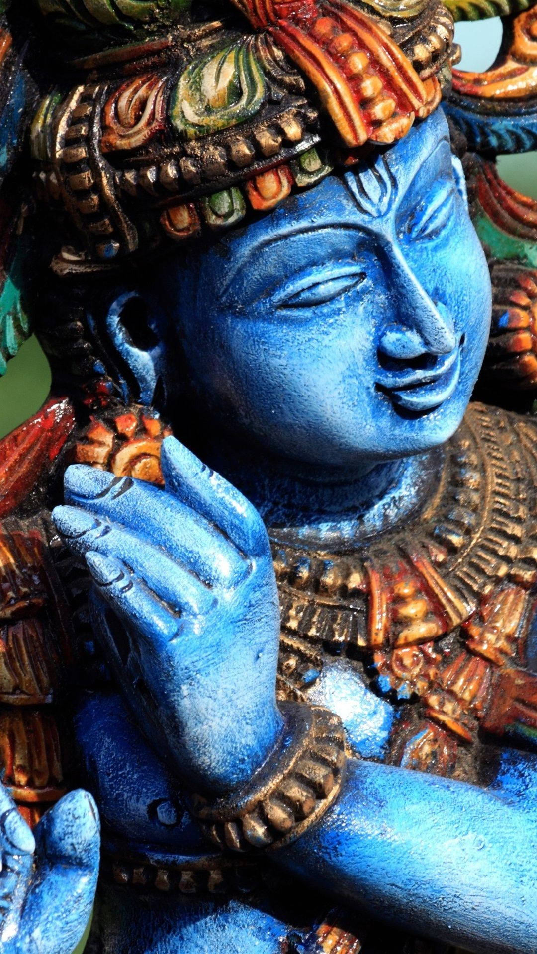 hindu iPhone 桌布 壁紙 — 寧靜藍皮膚神像的特寫，飾有精緻的金色和橙色珠寶以及華麗的頭飾。
