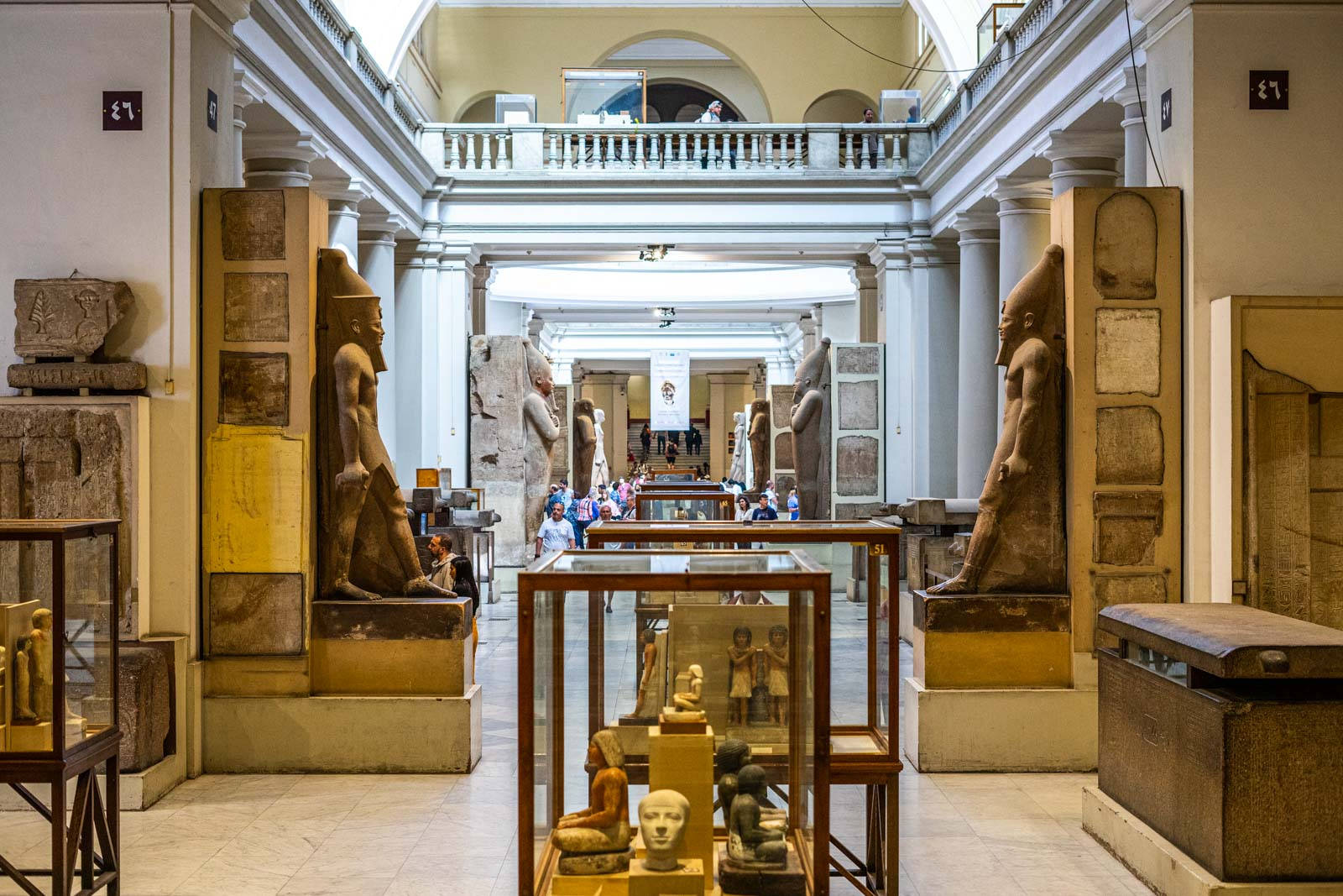 開羅 桌布 壁紙 — 寬敞的博物館大廳，高聳的古代雕像和玻璃展櫃在明亮的人造燈光下展示埃及文物。