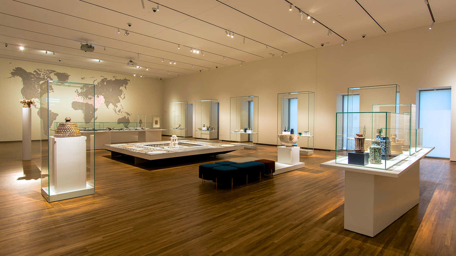 Aga Khan Museum 桌布 壁紙 — 寬敞的博物館畫廊，設有木地板、玻璃展示櫃和牆上的世界地圖壁畫，在明亮的頂燈下展示精選文物。