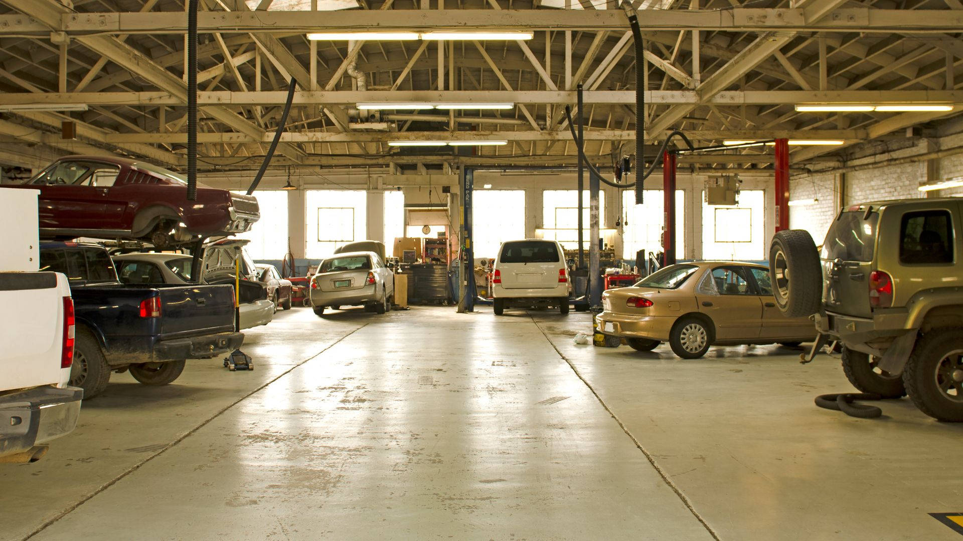 cars 桌布 壁紙 — 寬敞的汽車維修車庫，多輛車輛在升降機上和地板上，在明亮的螢光燈下。