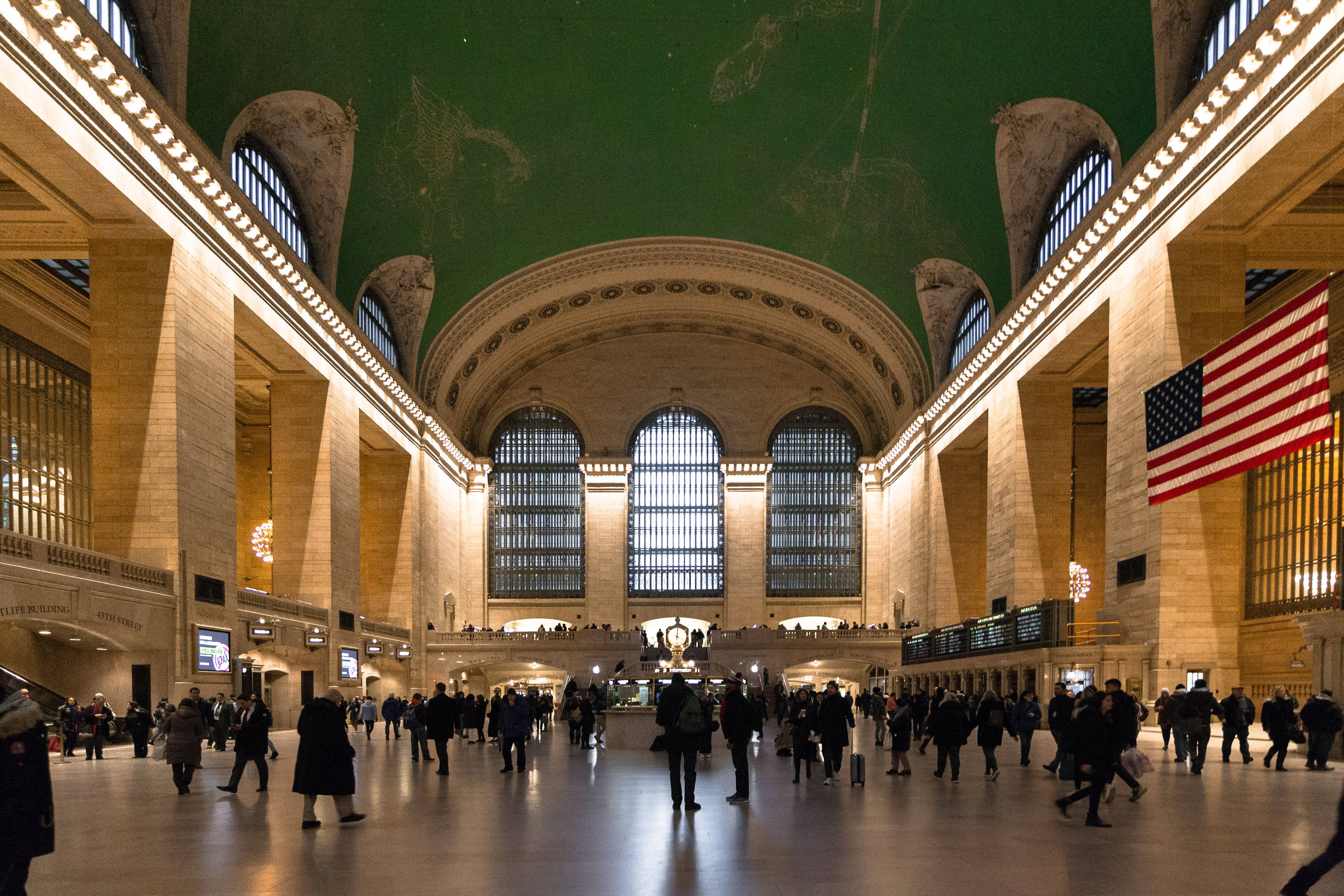 New York 桌布 壁紙 — 寬敞的火車站大廳，擁有高拱形天花板、綠色壁畫，以及旅客在溫暖金色燈光下穿梭。