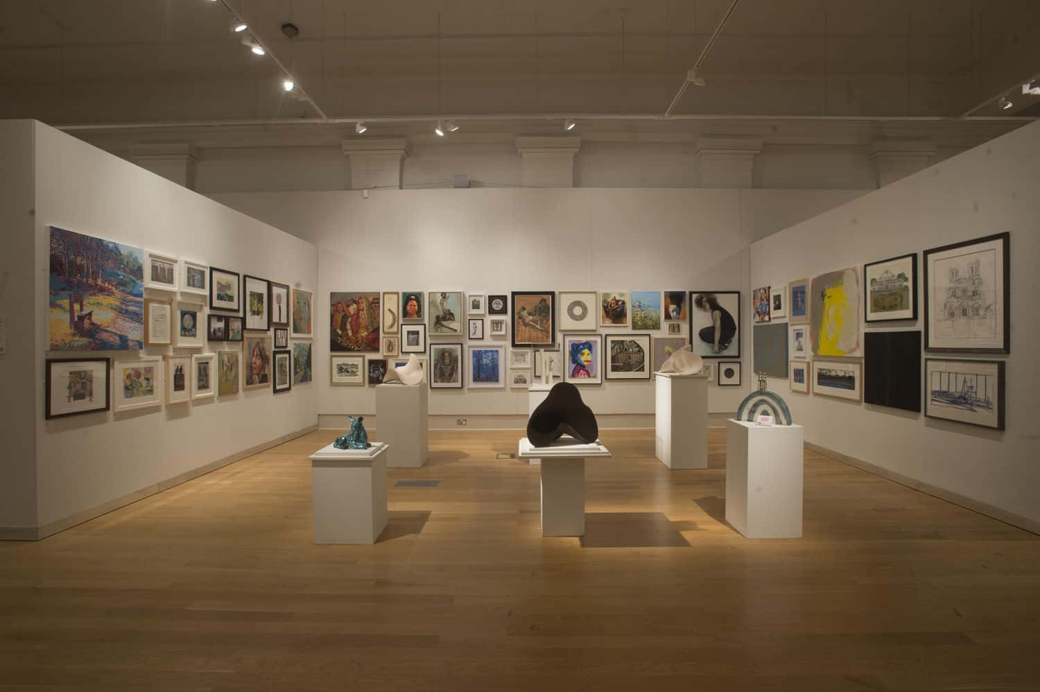 Exhibition 桌布 壁紙 — 寬敞的藝術畫廊，白色牆壁上掛滿了裱框畫作，白色底座上展示著雕塑，上方有溫暖的吊燈照明。
